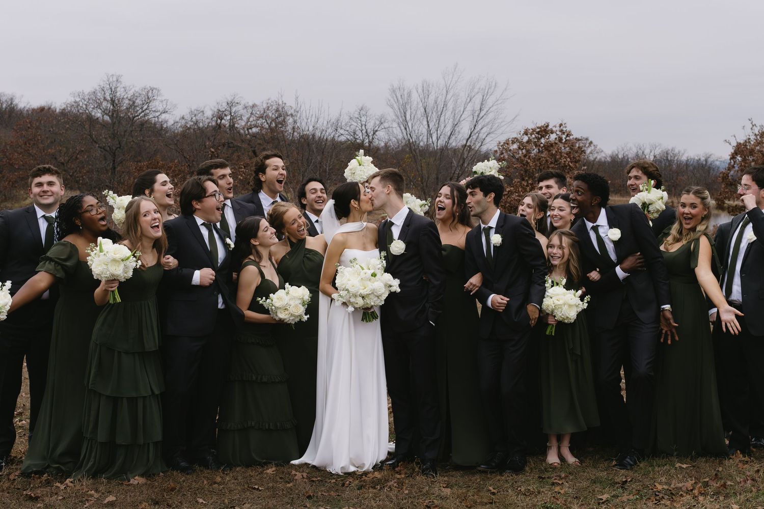 A wedding party in black and white attire poses together on a cloudy day.