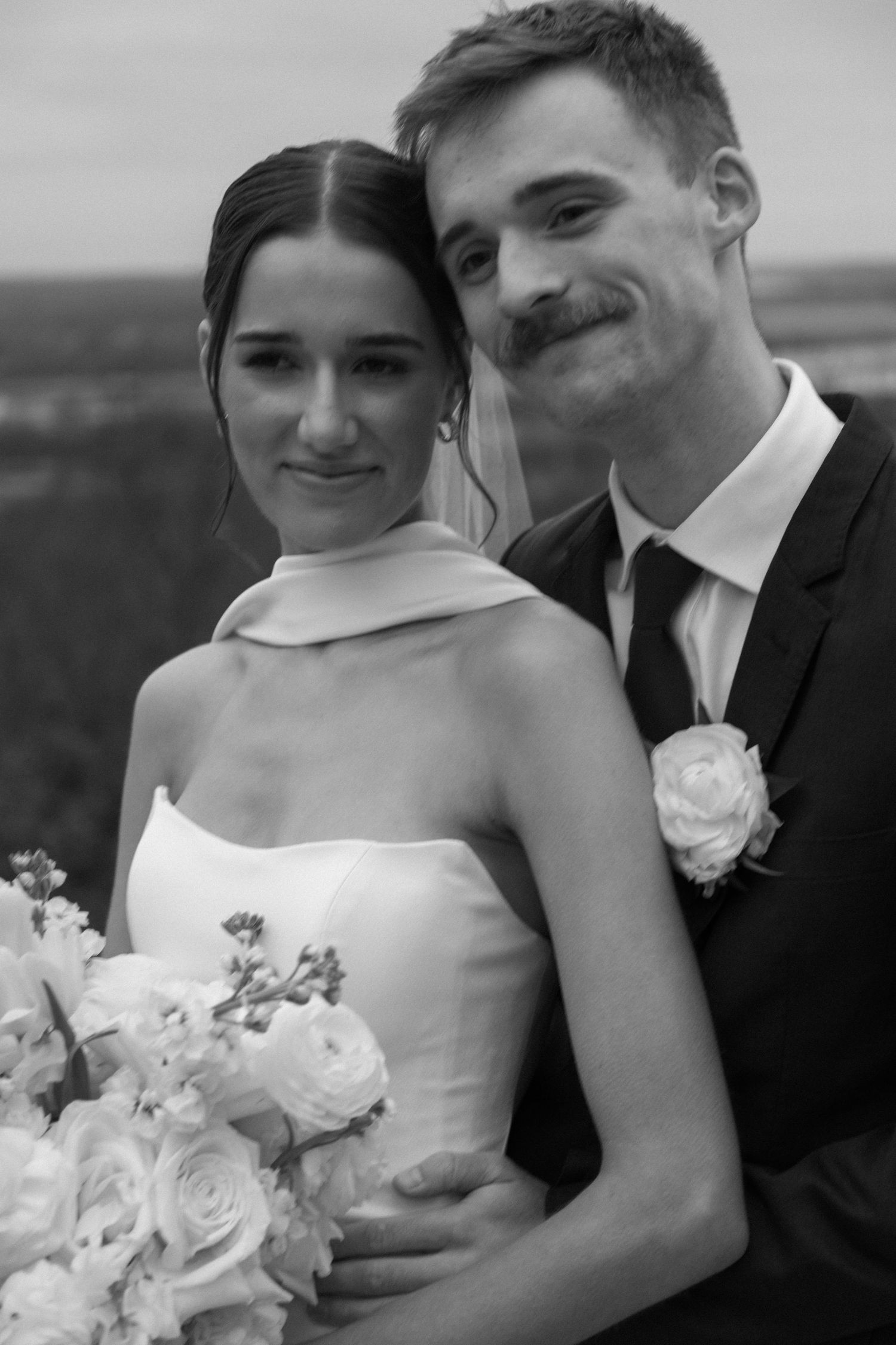 A black and white portrait of newlyweds with white roses.