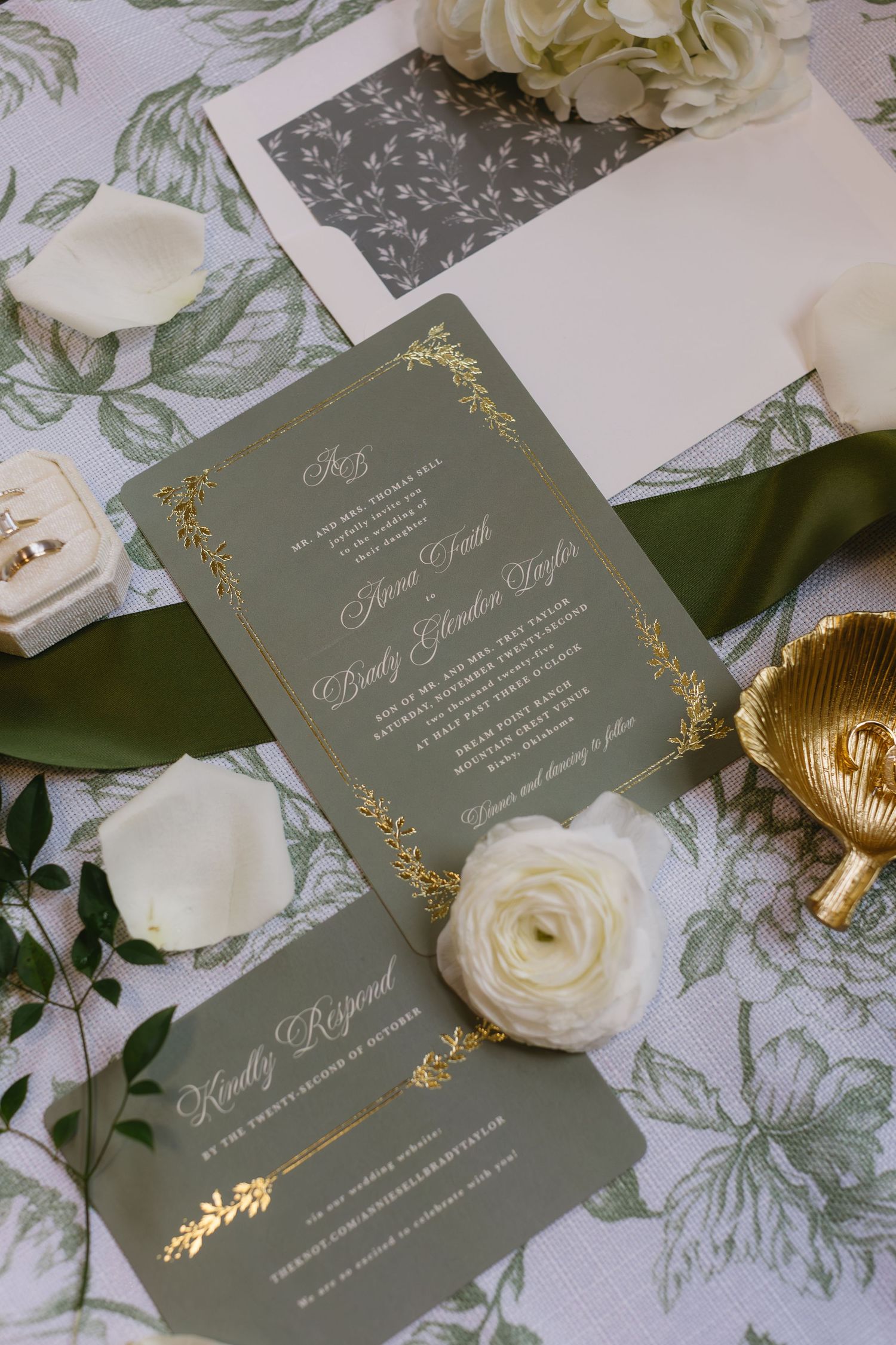 Elegant wedding invitations in gray with gold foil details and white flowers on a floral patterned background.
