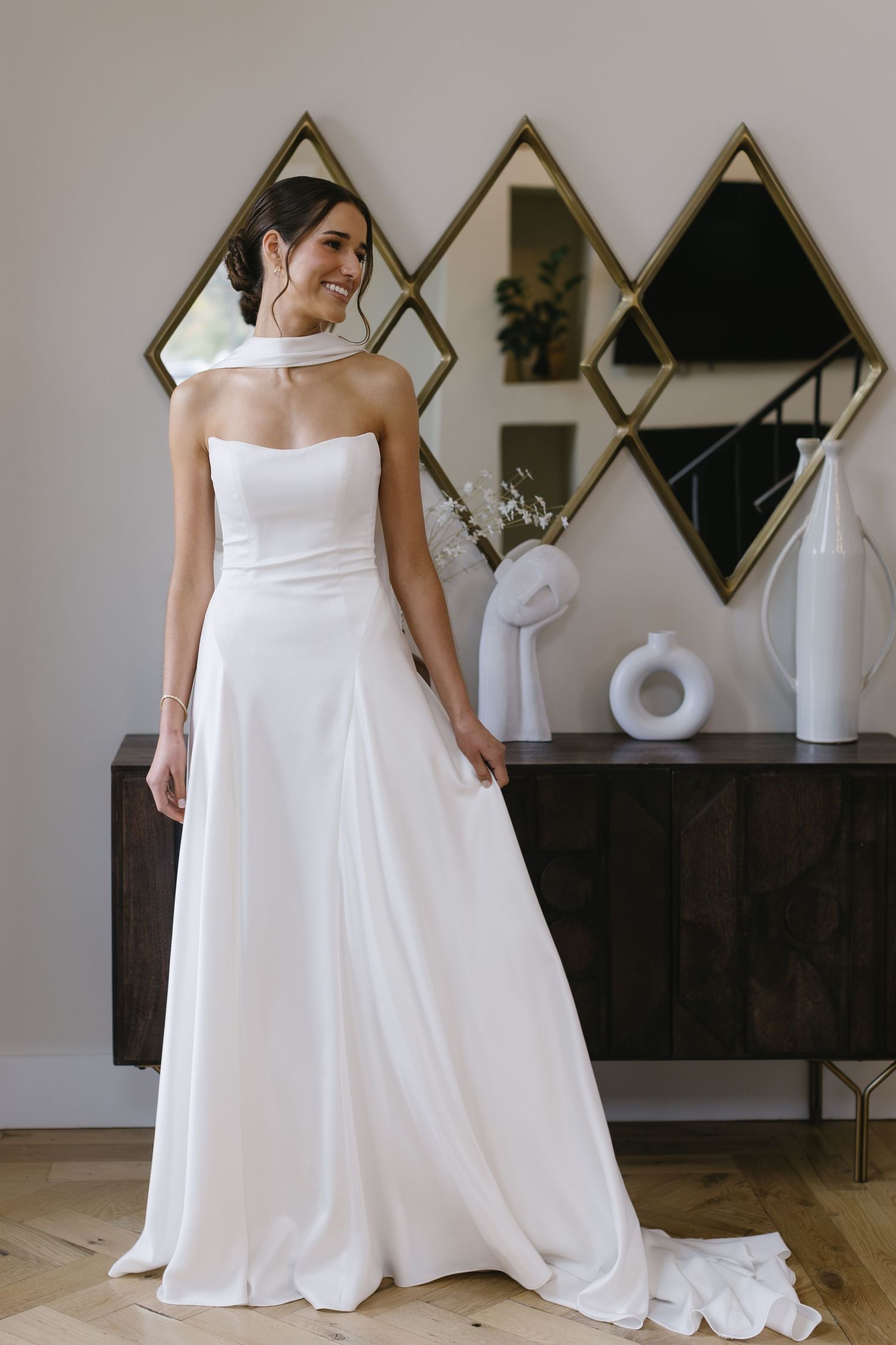 White wedding gown with flowing train displayed in a modern room with geometric wall decor.