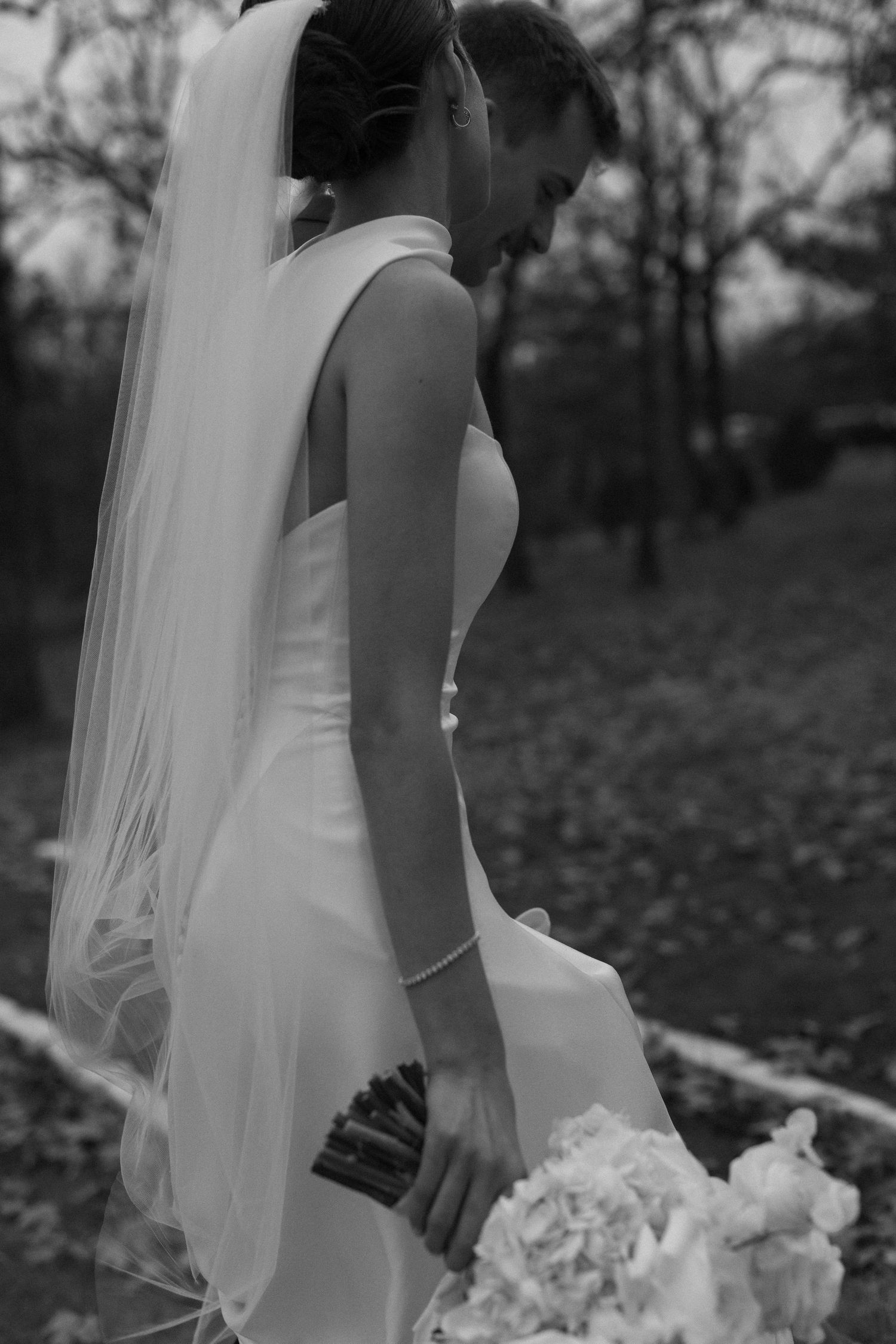 A bride in a white dress and veil holds a bouquet during an outdoor wedding photoshoot.