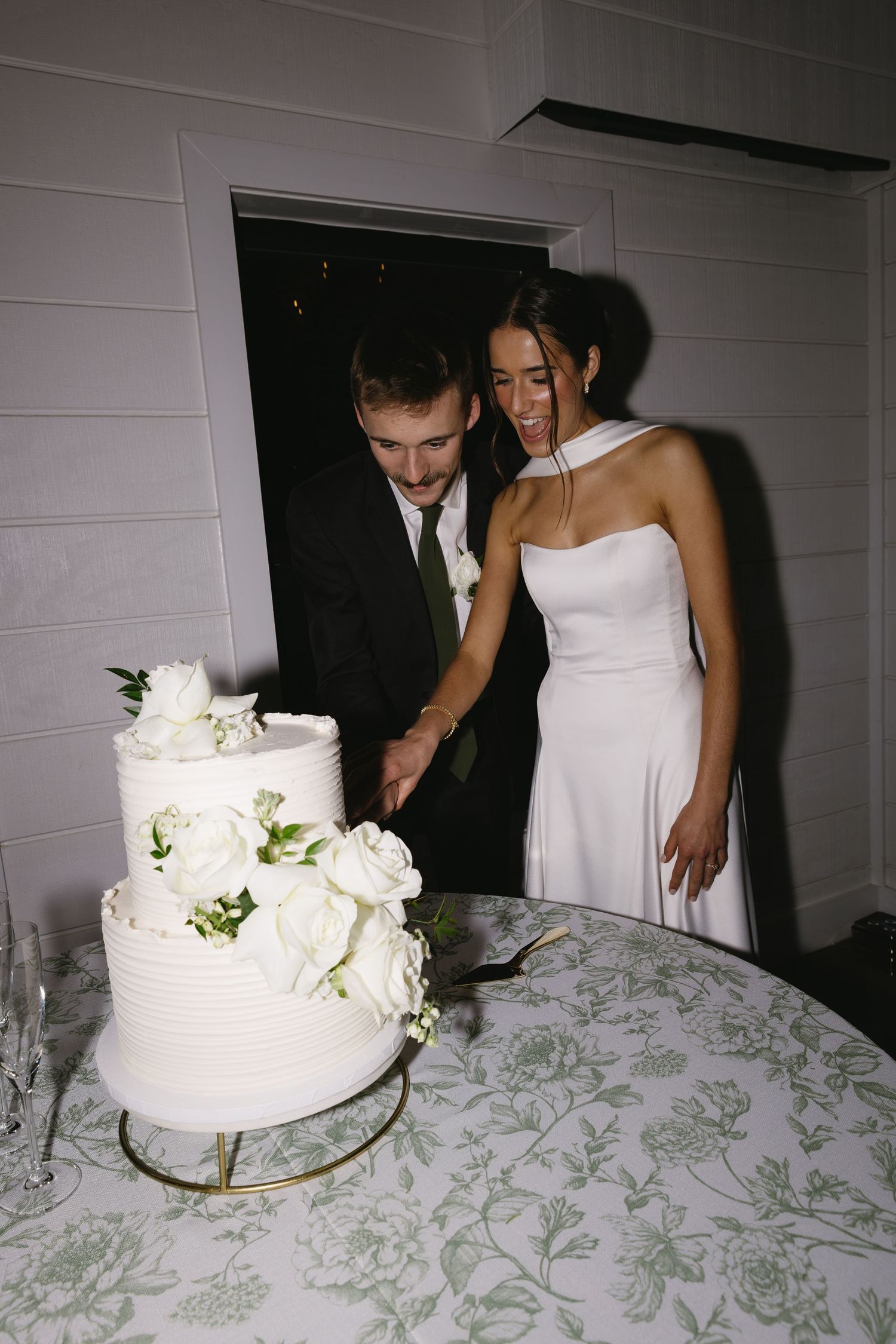 A couple cutting their white floral wedding cake together at their reception.