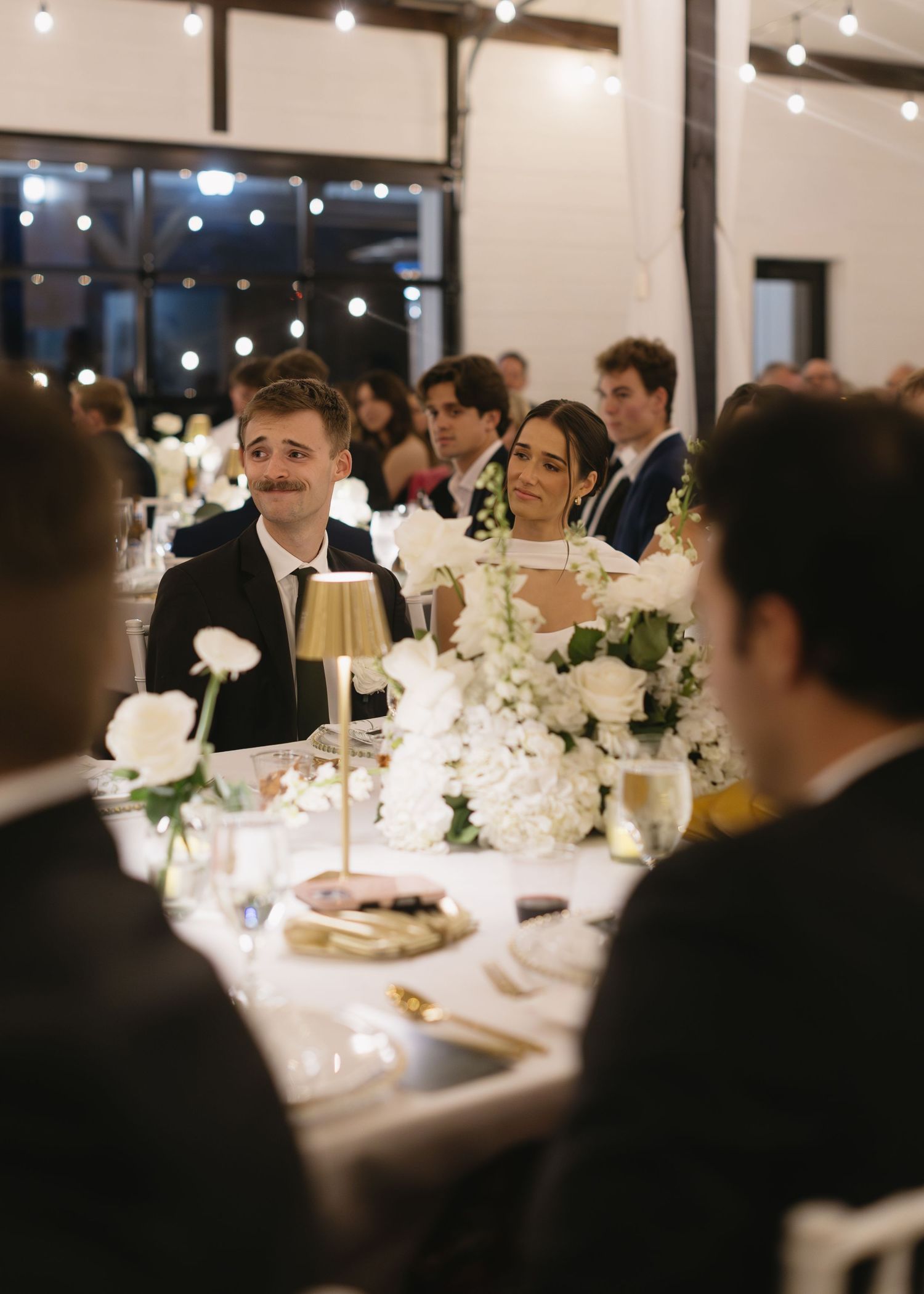Wedding reception dinner scene with guests seated at elegantly decorated tables.