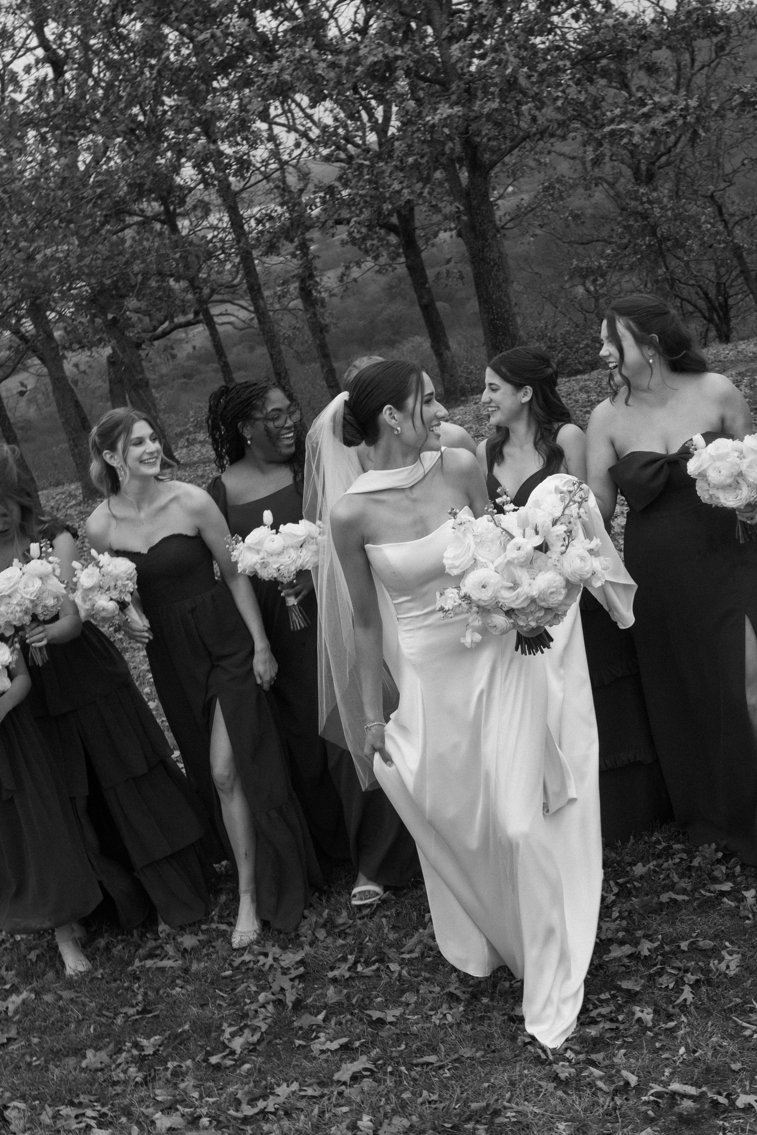 Wedding party in contrasting black and white attire posing together on fallen autumn leaves.