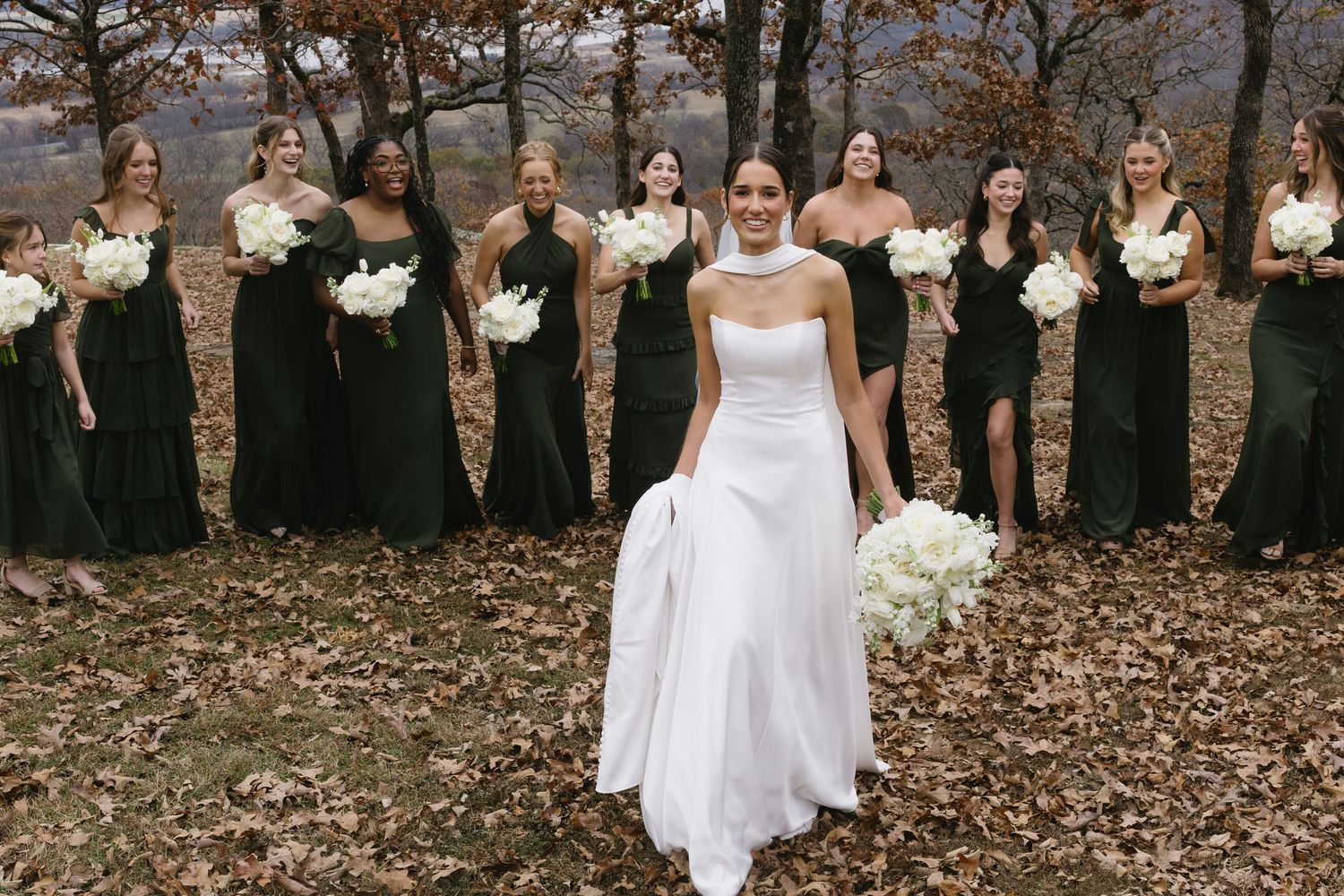 Wedding party in black dresses and white gown standing in line during fall season.