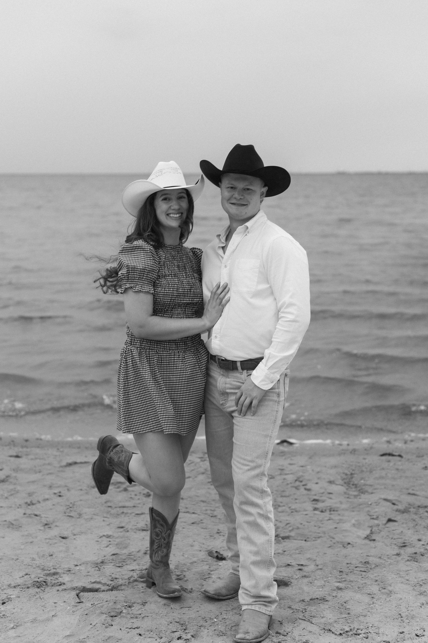 Playful couple in western attire enjoying moments together on a beach.