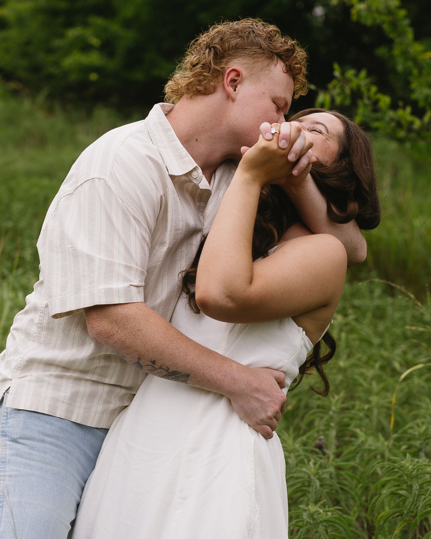 A couple in white clothing share tender romantic moments in a scenic outdoor field setting.