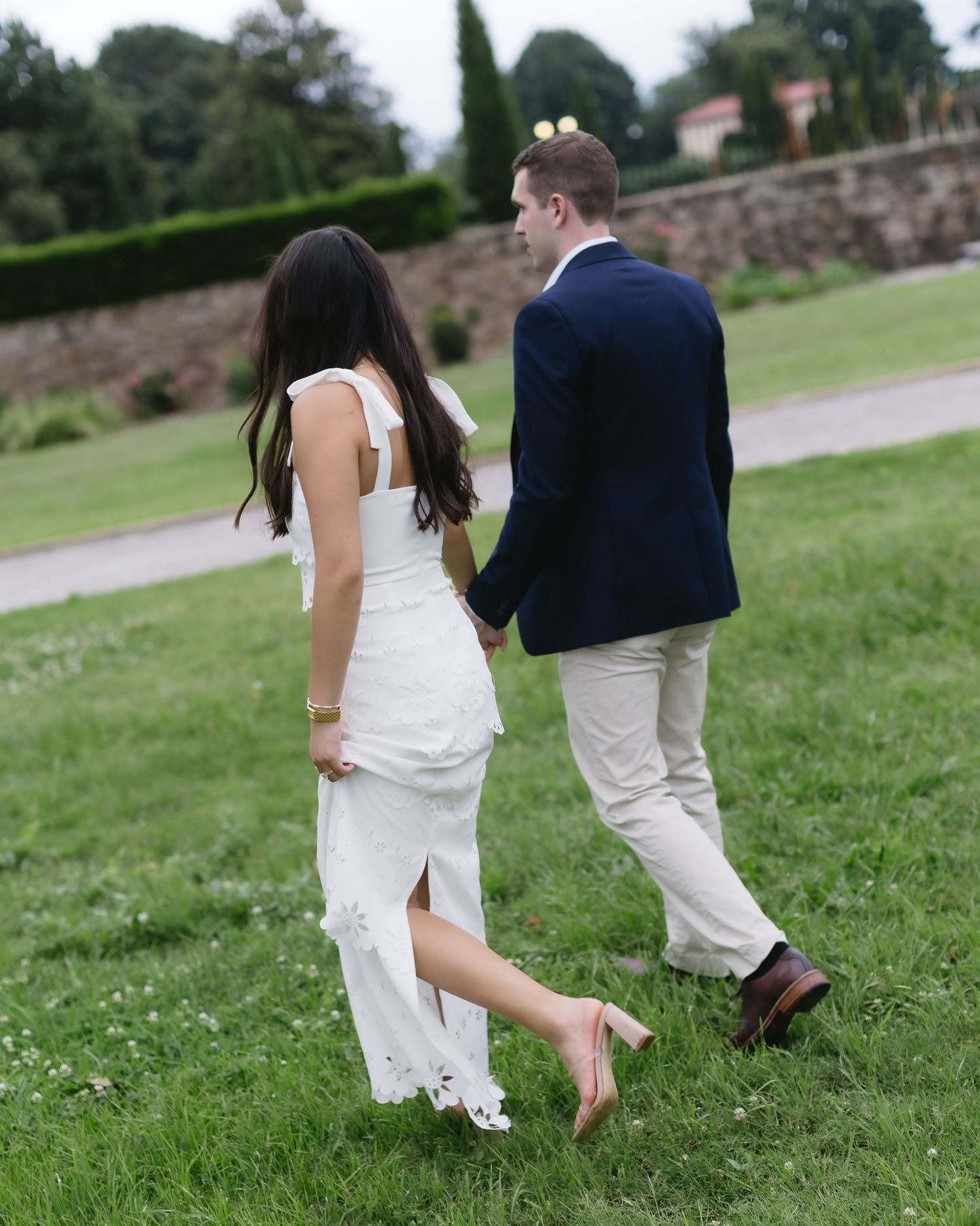 Couple in wedding attire walking playfully through grass during outdoor photo session.
