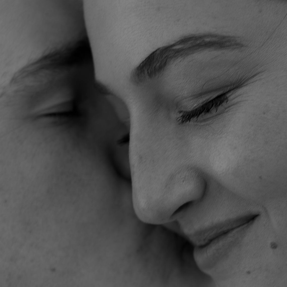 A tender black and white close-up photograph showing an intimate moment between two people.
