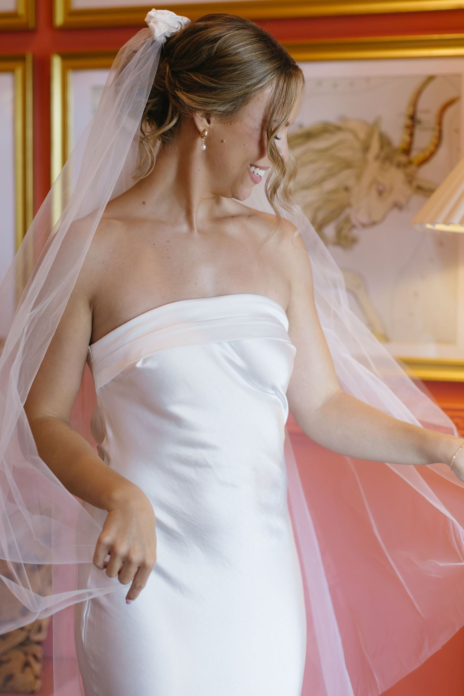 Elegant bridal portrait with flowing veil against ornate red and gold wallpapered room.