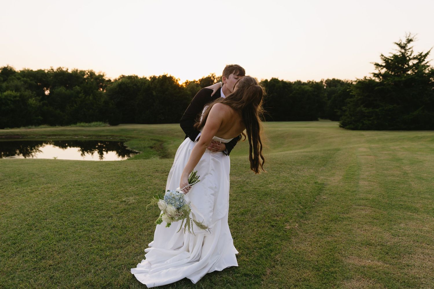 Wedding couple walking and dancing together on a grassy field at sunset.
