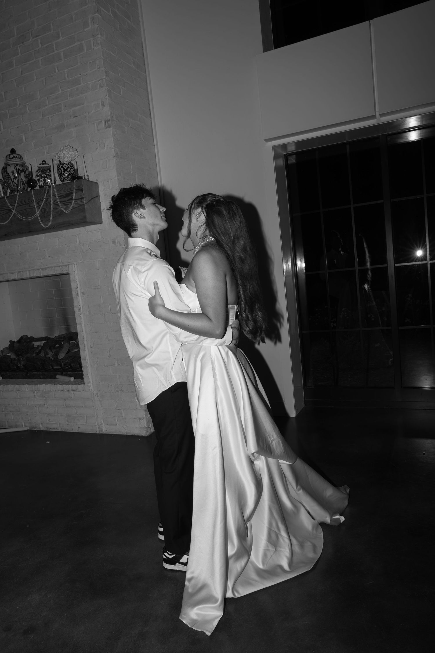 A romantic couple dancing in black and white photography in a darkened indoor space.
