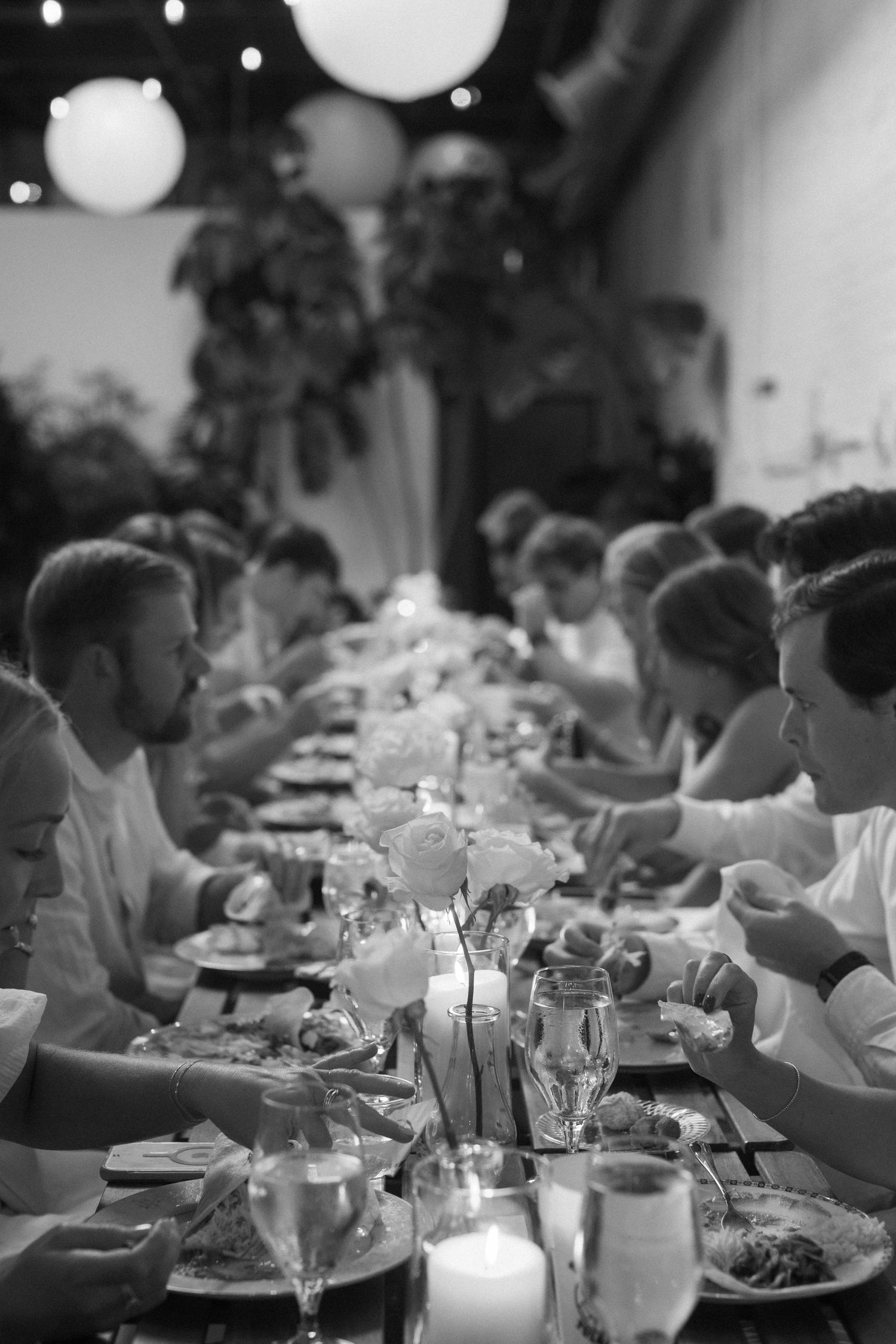 A black and white image of guests dining at an elegant reception with round tables and candlelight.