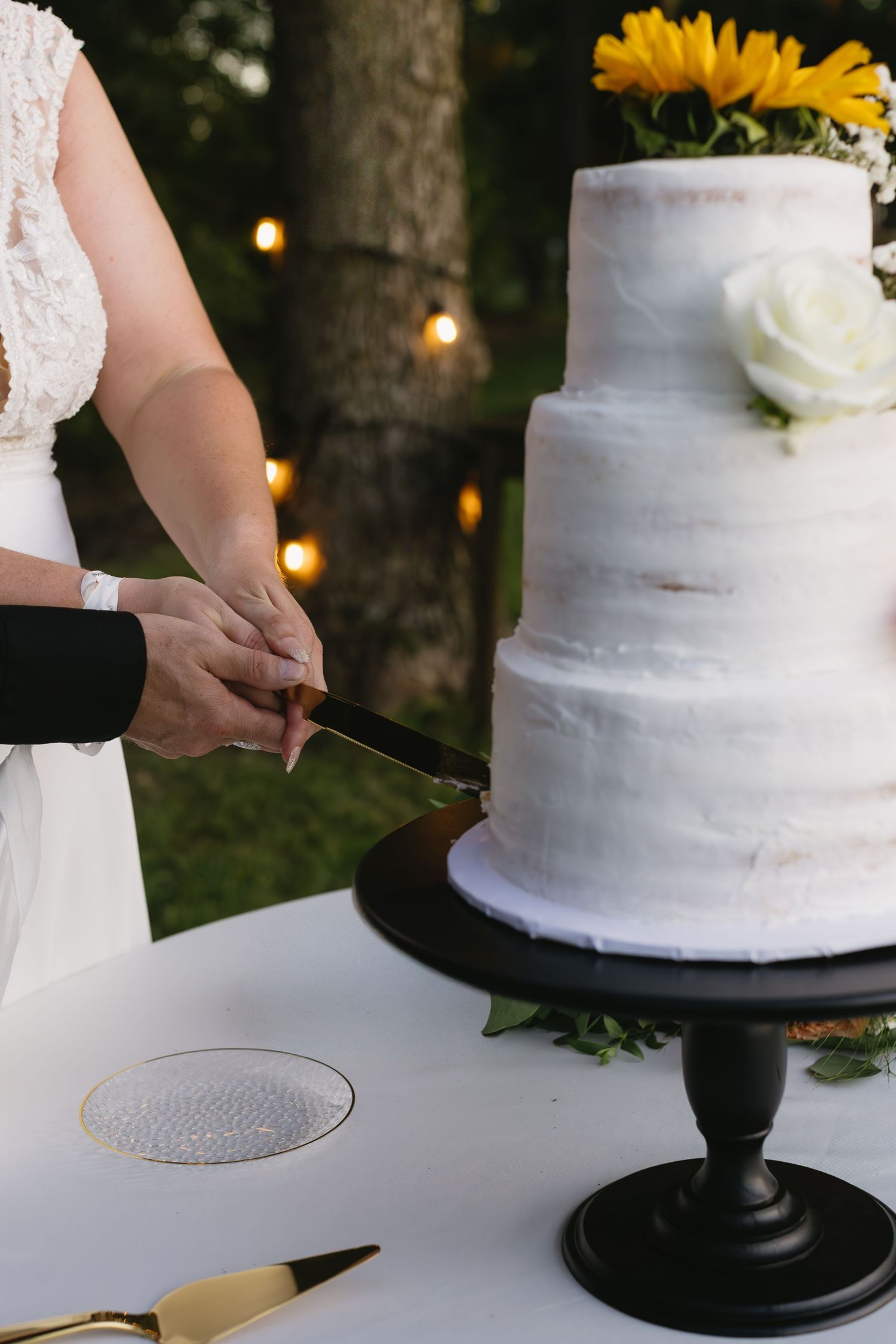 A white wedding cake with floral decorations being prepared on a black cake stand.