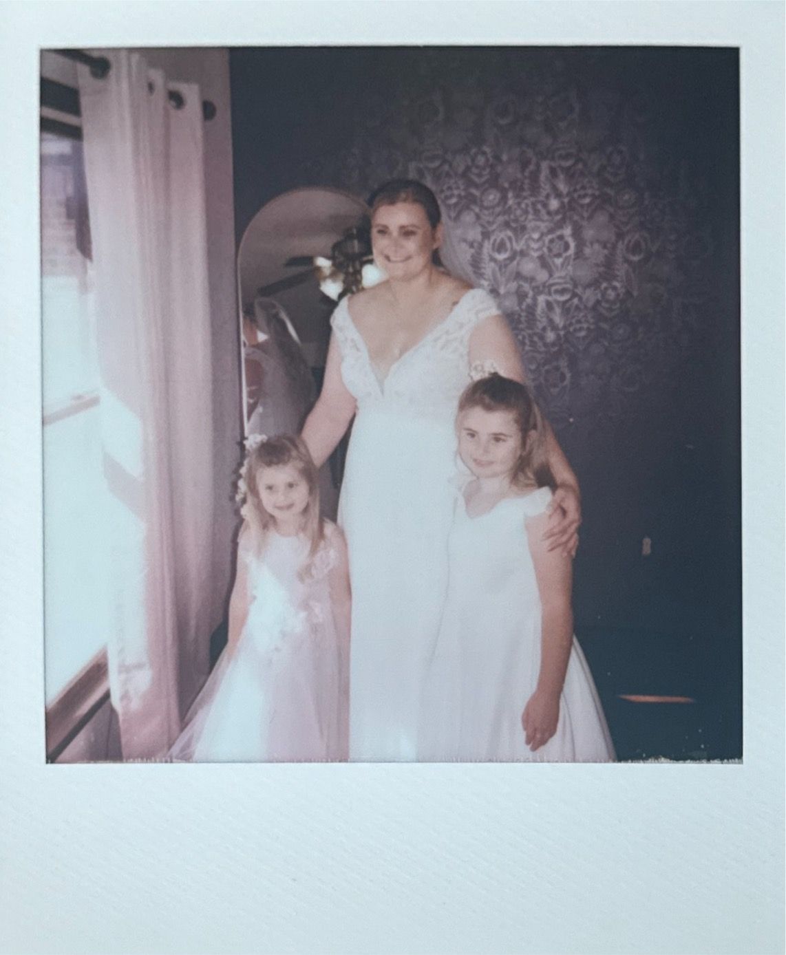 Bride and bridesmaids in white dresses getting ready in an elegant room with decorative wallpaper.