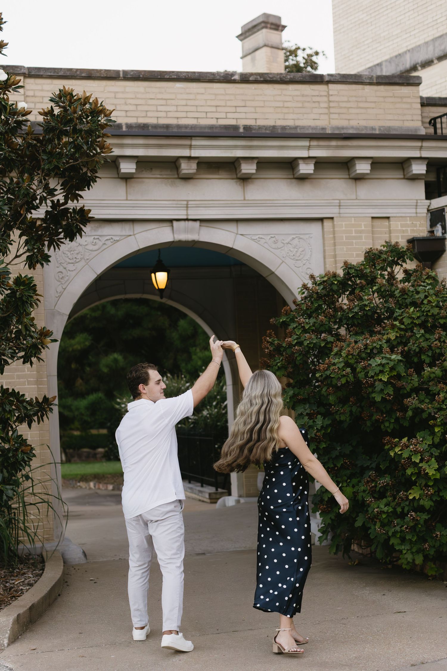 Couple dancing and twirling under stone archways on a paved courtyard.