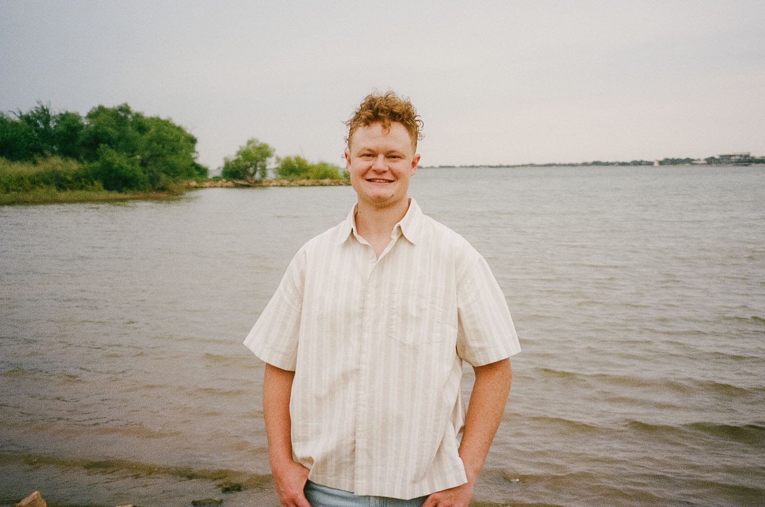 A person standing by a calm river or lake on an overcast day.