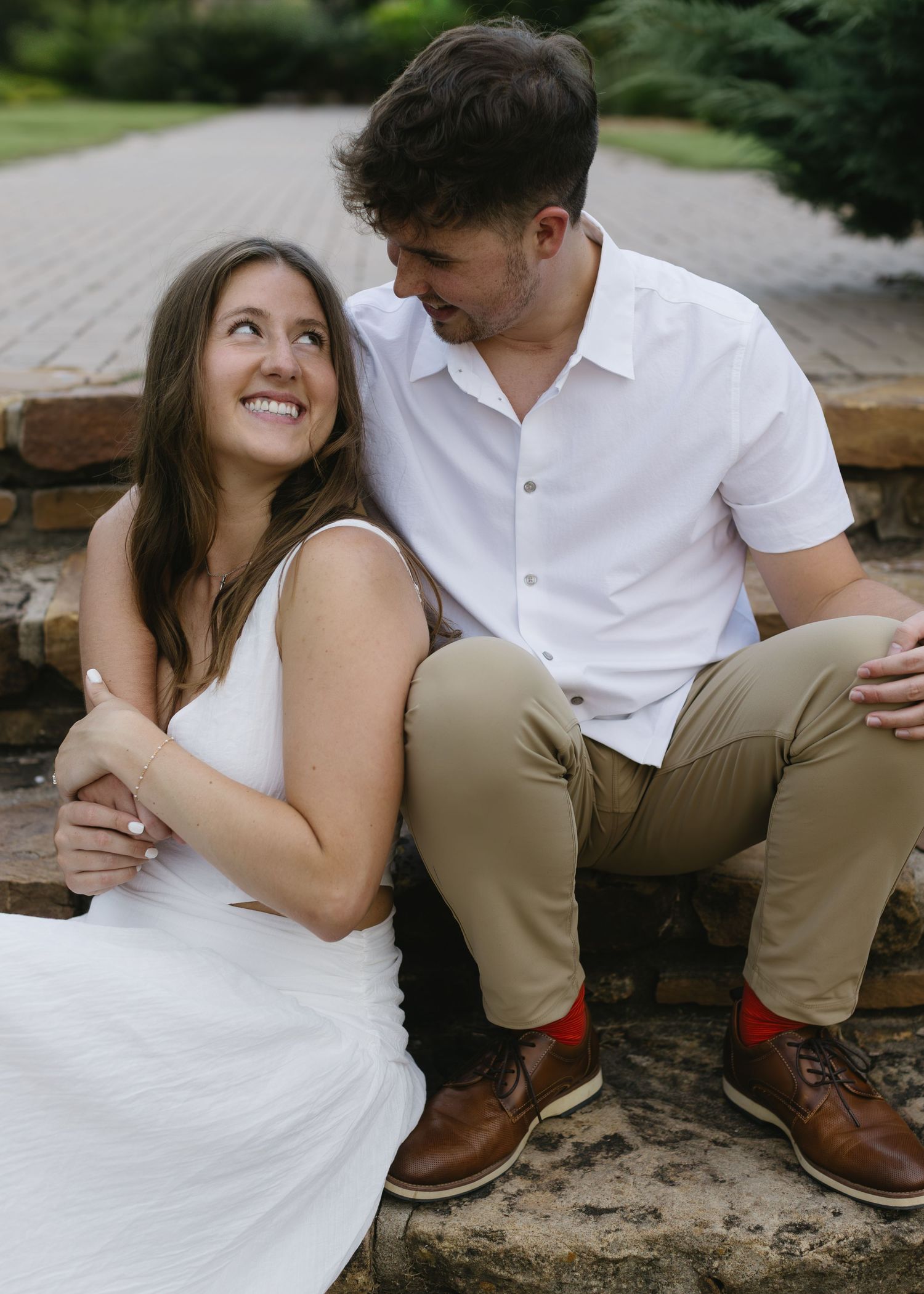 A couple in casual attire poses intimately on a stone wall during an outdoor photoshoot.