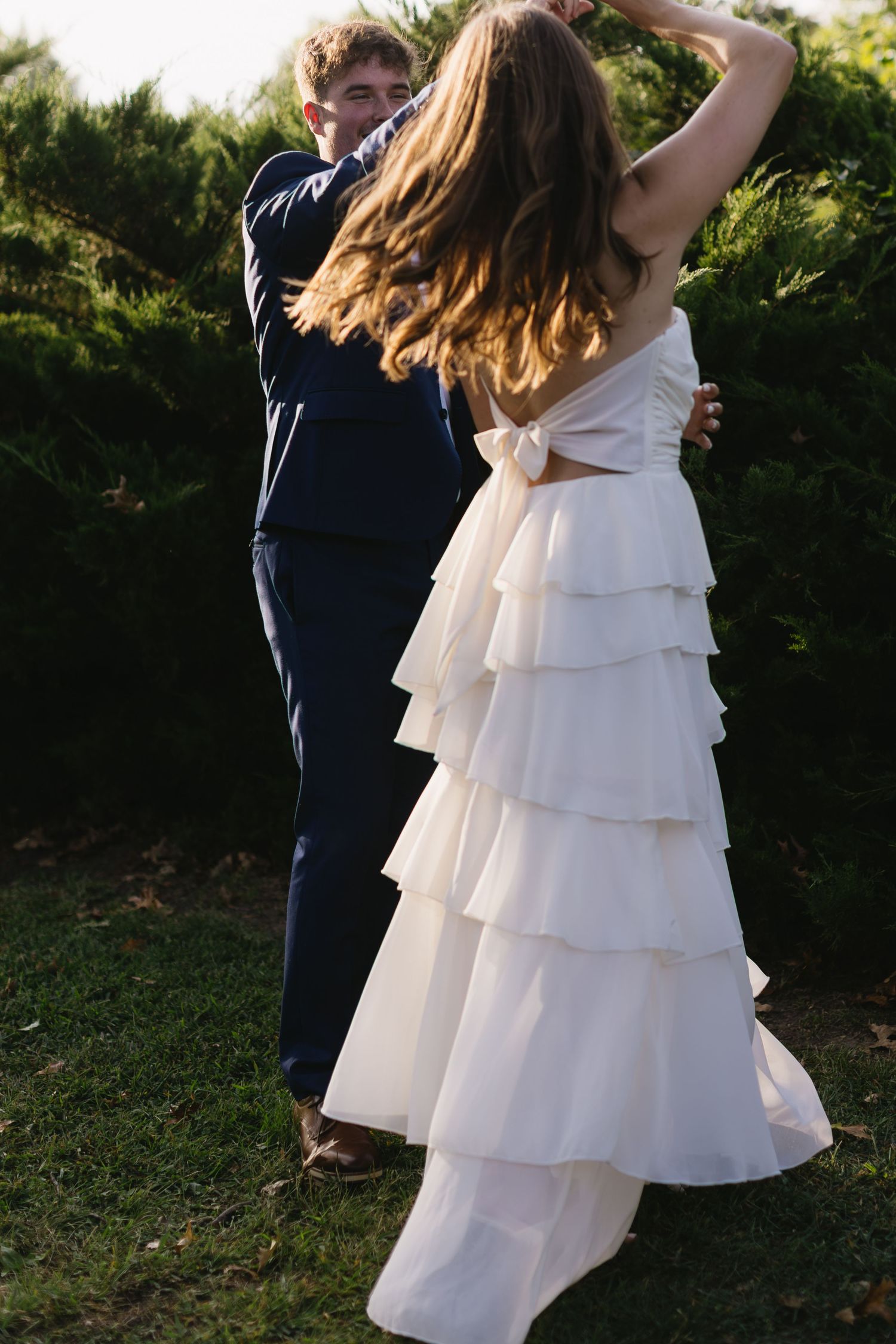 A couple in wedding attire dances together outdoors, with the bride wearing a white layered dress.