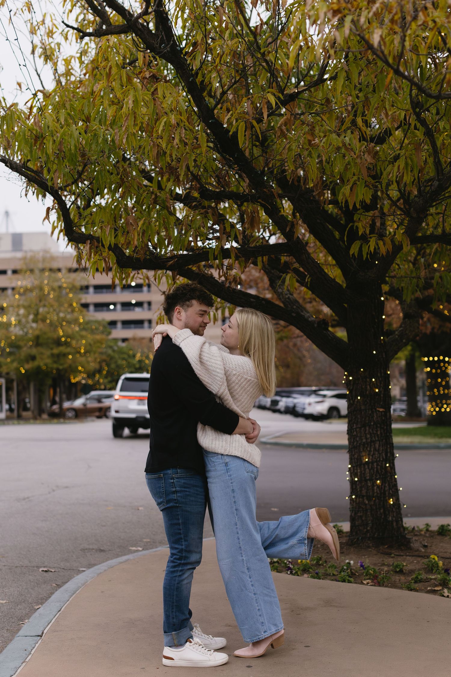 Romantic couple embracing under autumn trees in an urban parking lot setting.