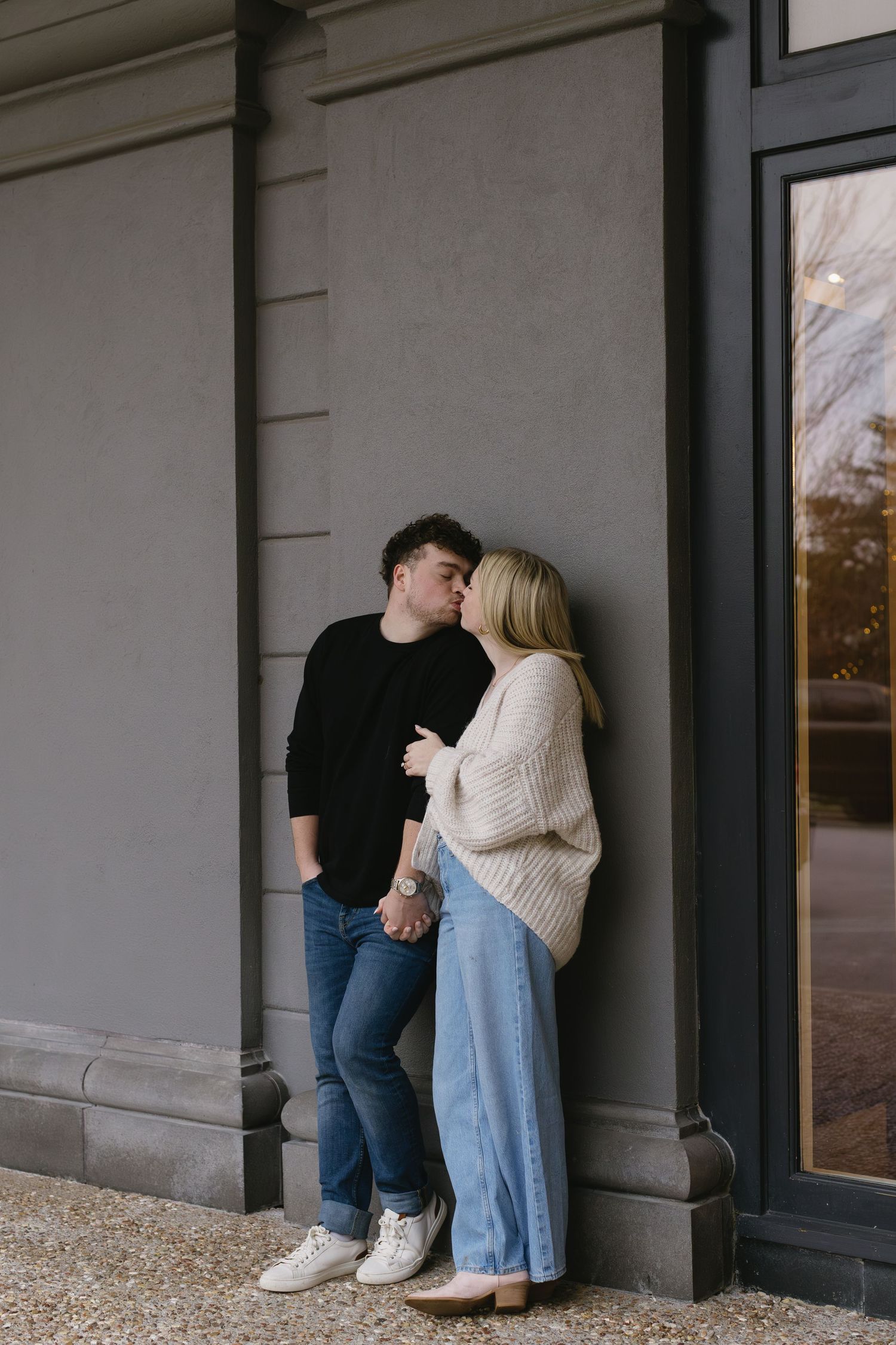 Couple sharing a tender moment against a grey wall in casual winter clothing.