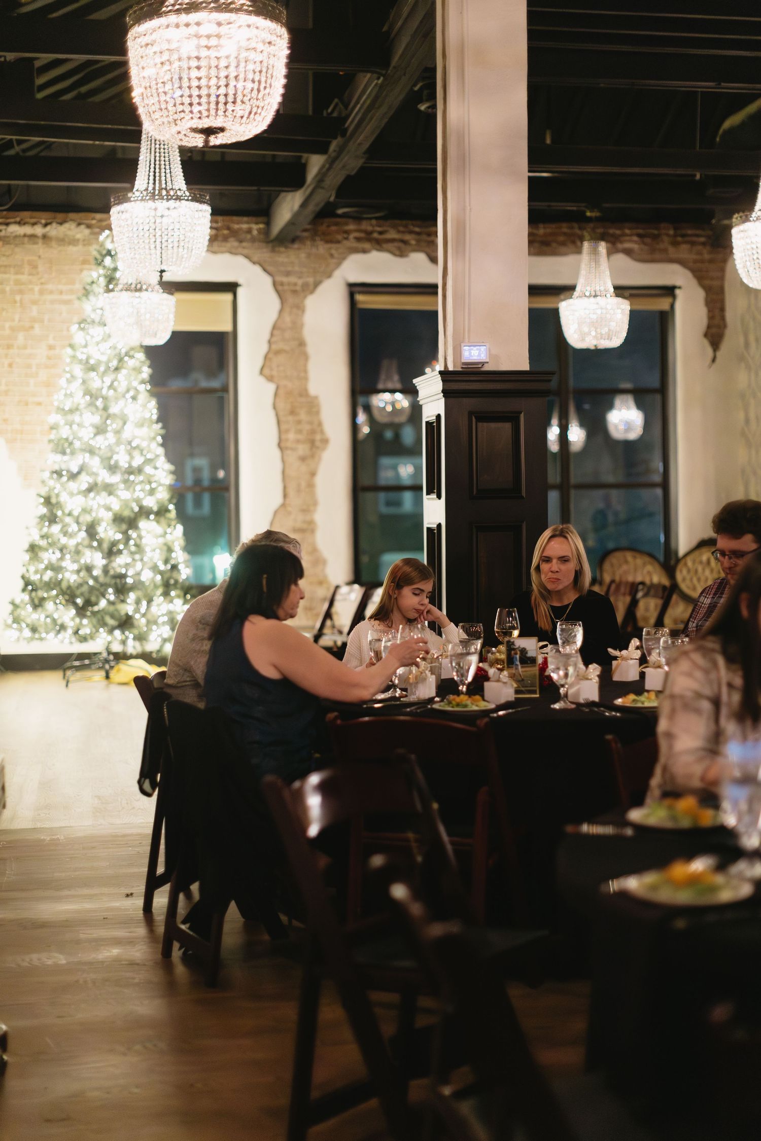 Guests dine under crystal chandeliers in a rustic-elegant venue with exposed brick walls.