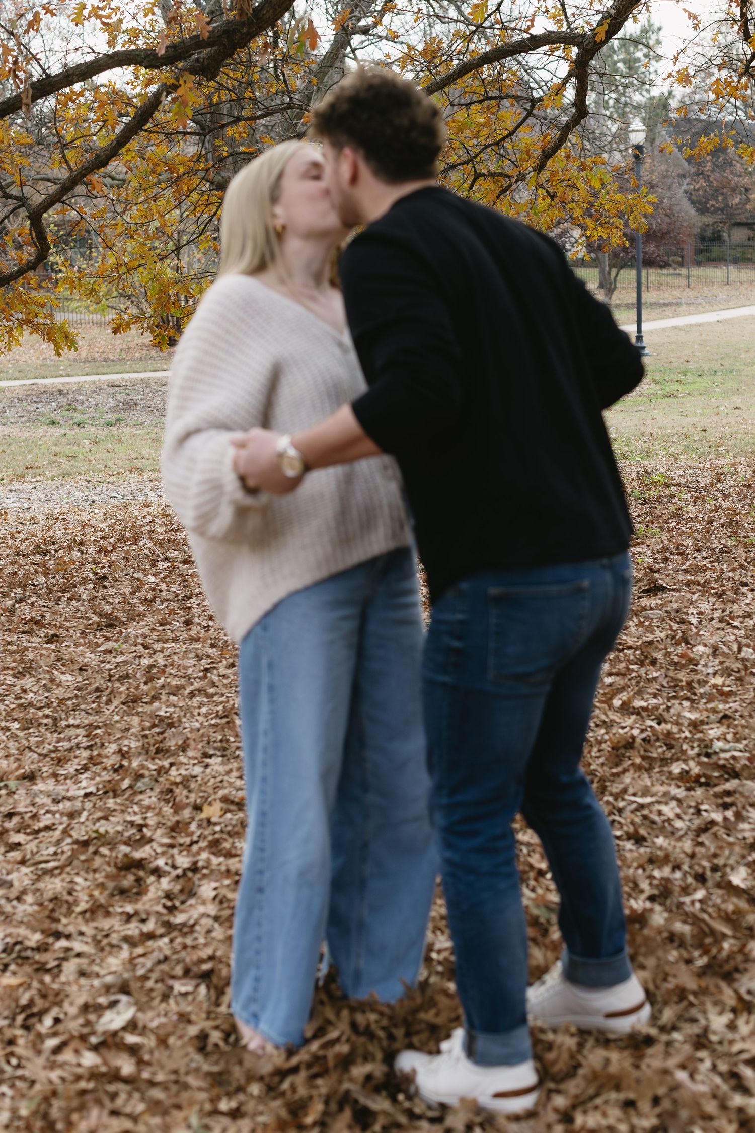A romantic autumn moment captured as a couple embraces under golden leaves in a park.