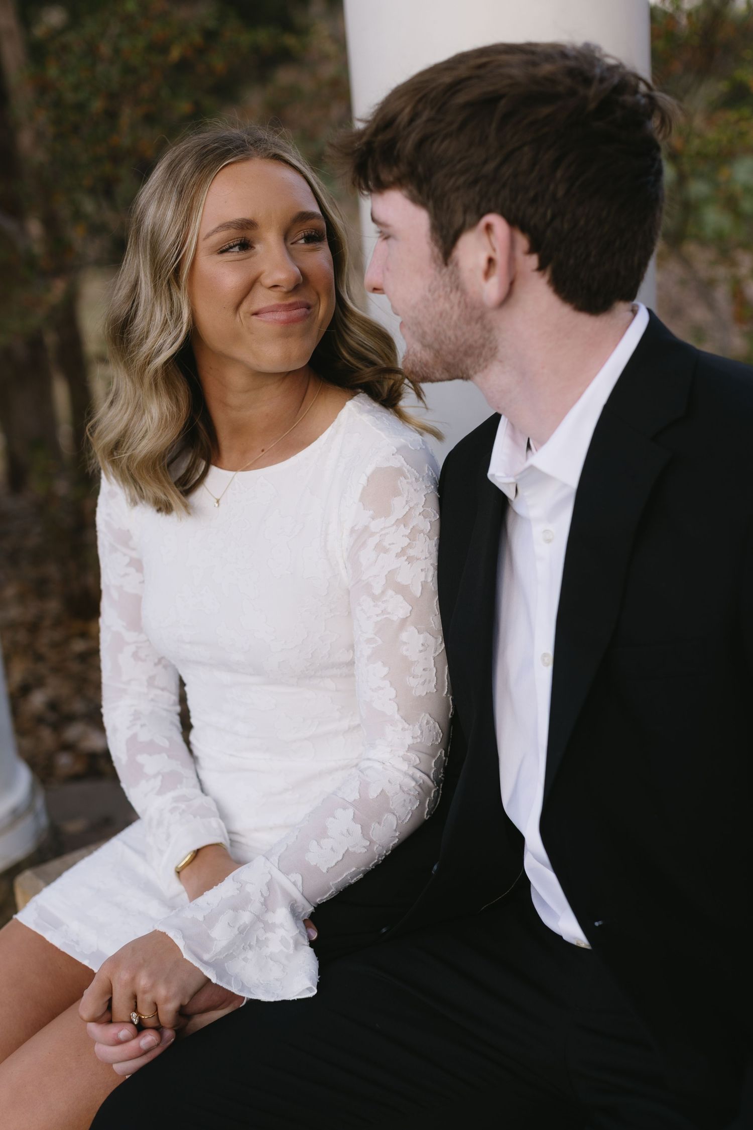 Couple in white and black formal wear sitting together under a columned portico.