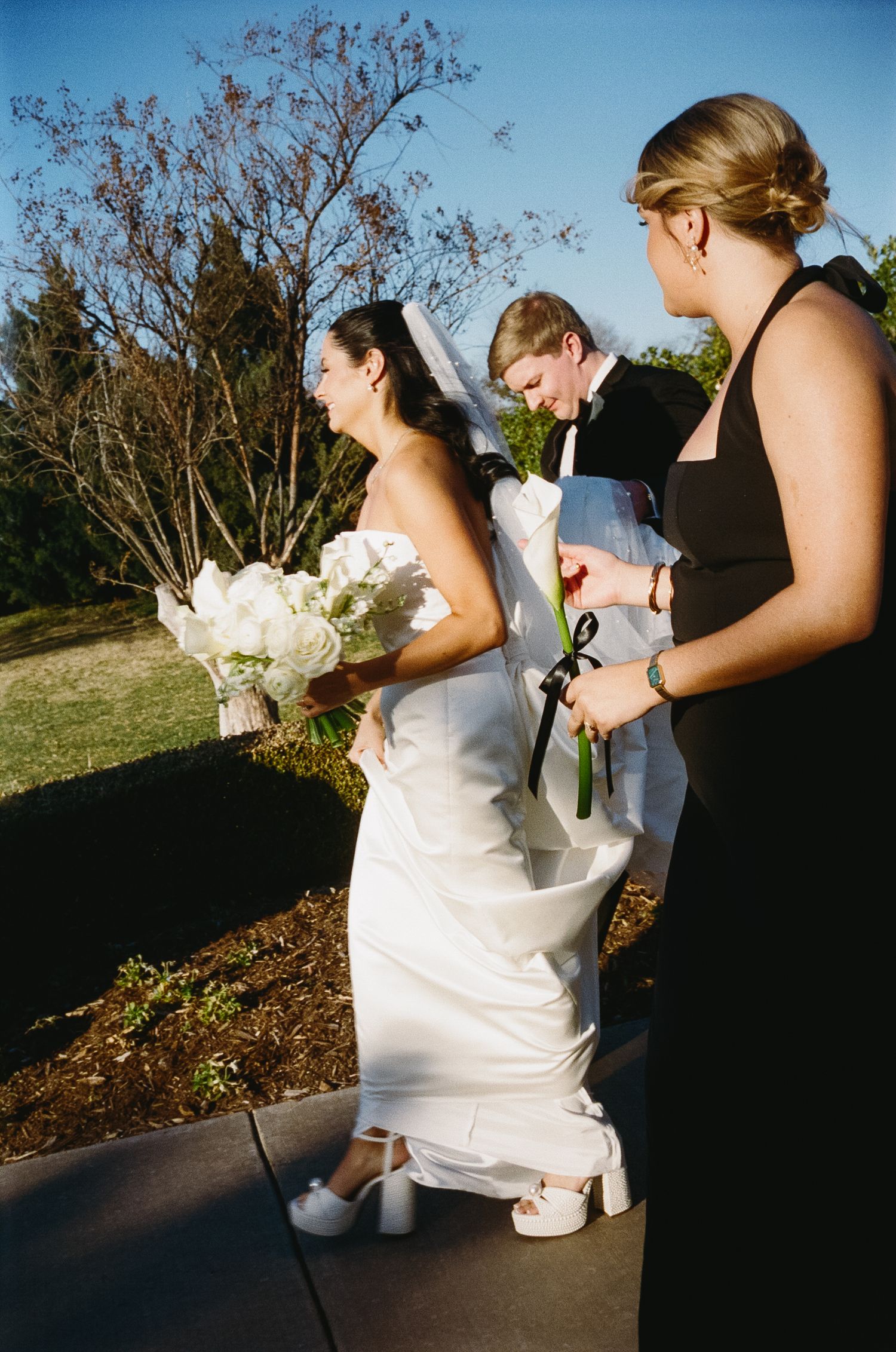 Wedding party in formal attire holding bouquets outdoors during sunset.
