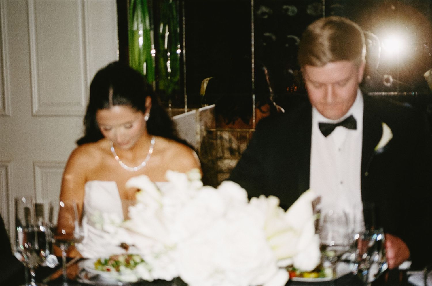 Wedding reception dinner table with white floral centerpiece and formal place settings.