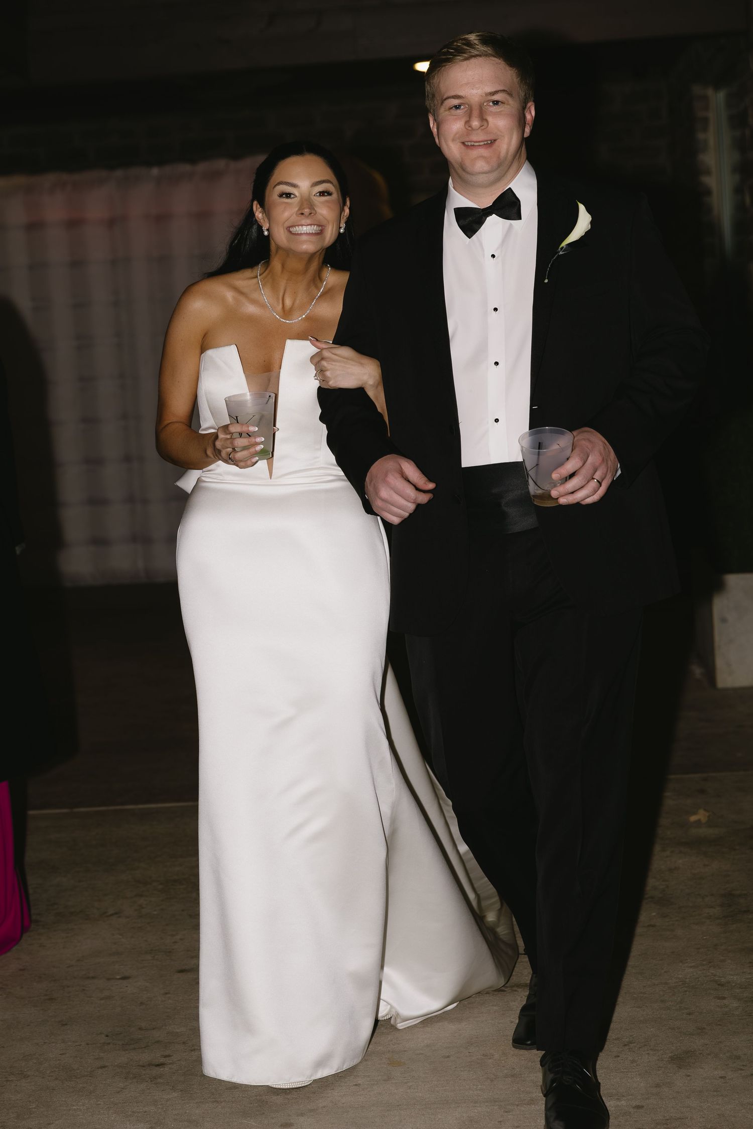 Couple in formal wedding attire walking together at night.