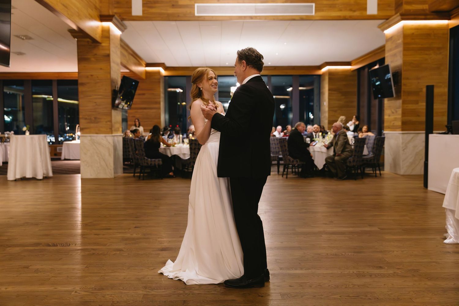A spacious wooden-floored ballroom set up for a wedding reception with elegant lighting.