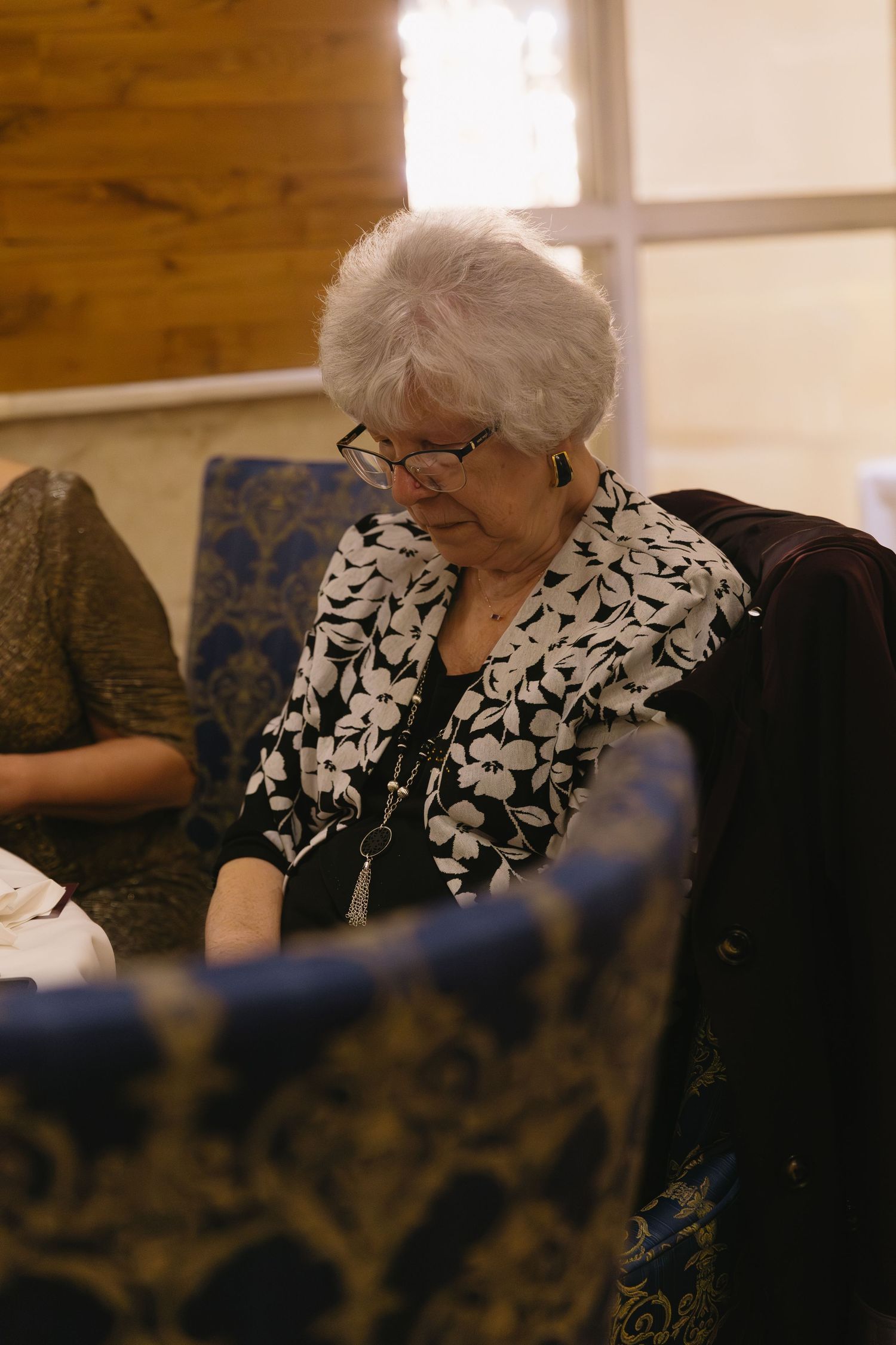 Wedding guests in formal attire seated at tables during an indoor reception.