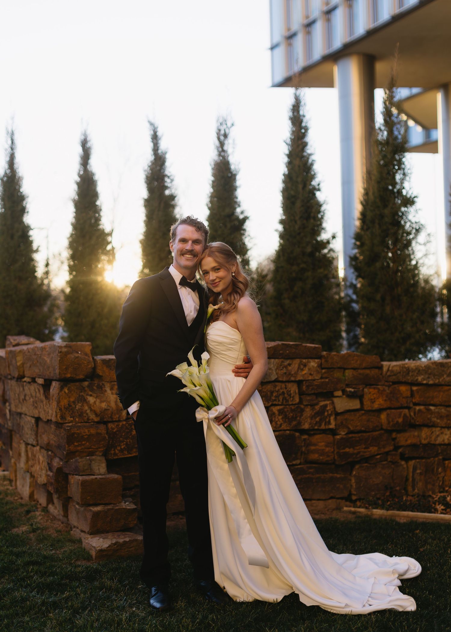 Sunset wedding portrait session with stone wall and cypress trees in the background.
