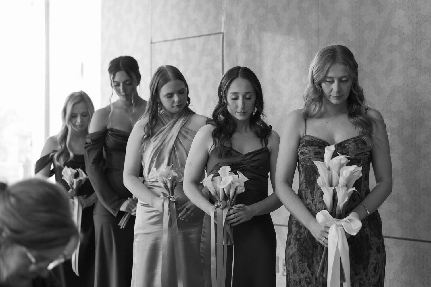 Row of bridesmaids in dark dresses hold bouquets during formal wedding photos.