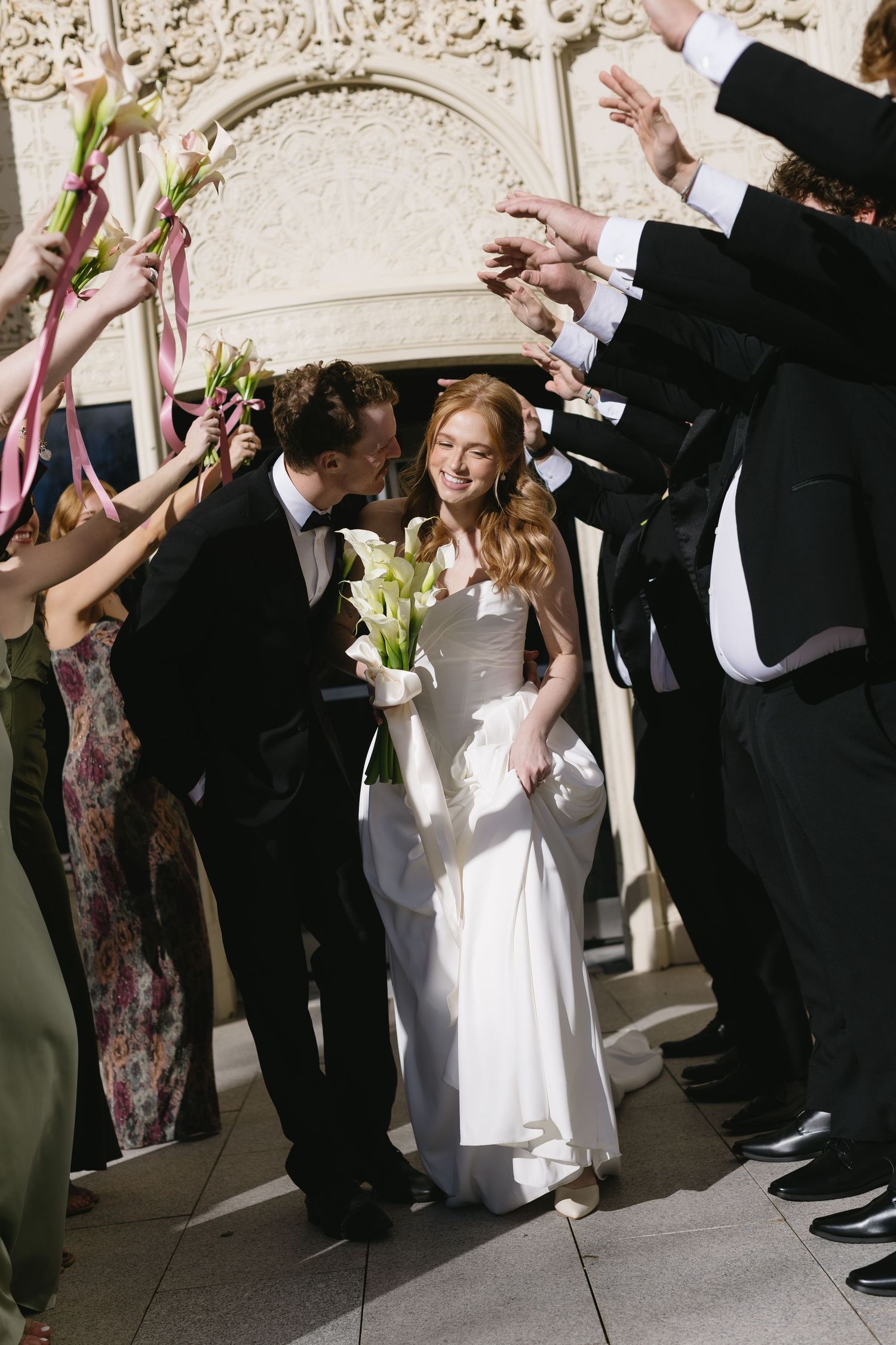 Wedding party members gather for candid photos against an ornate stone wall backdrop.