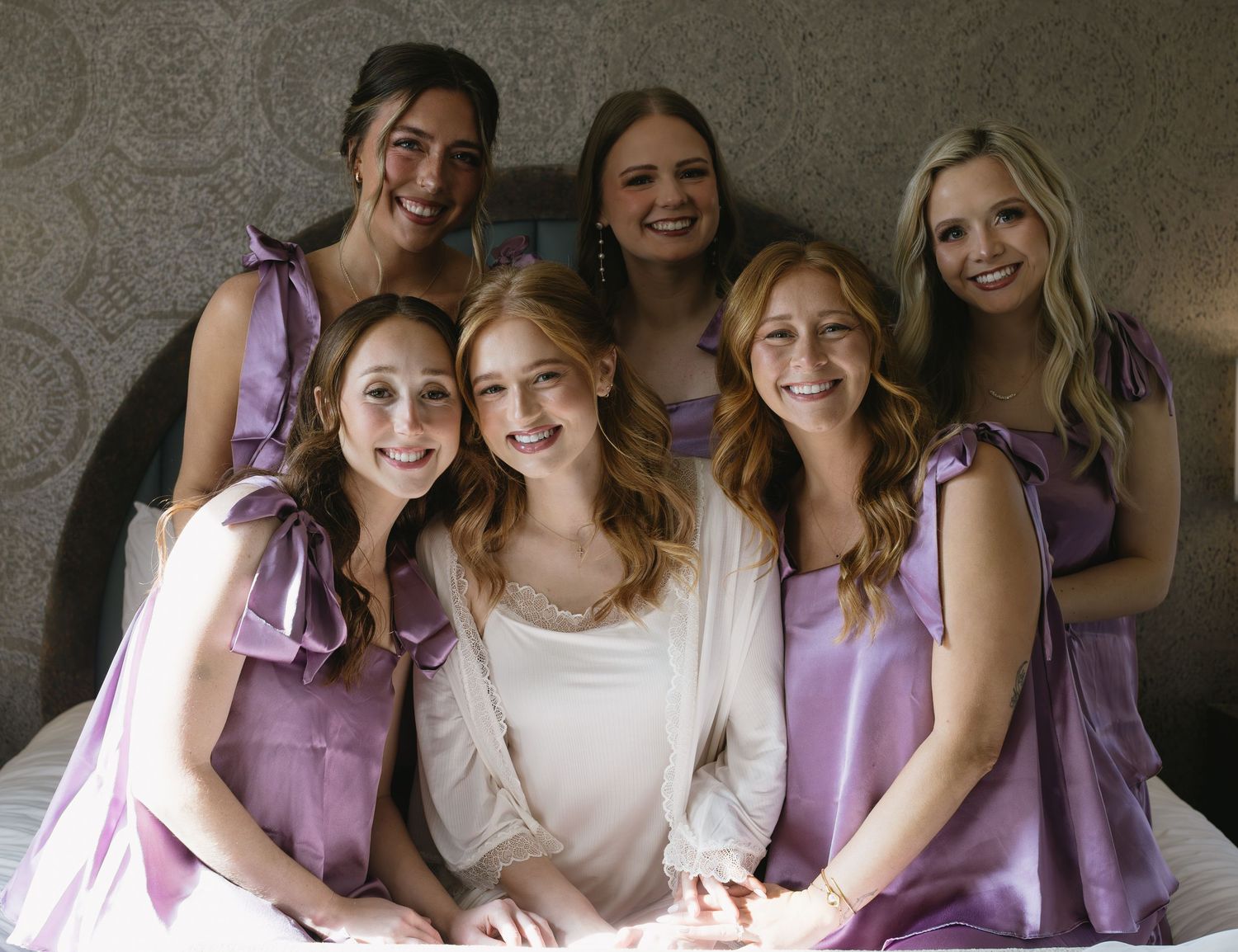 Wedding party wearing purple bridesmaid dresses and white bridal gown posing together.