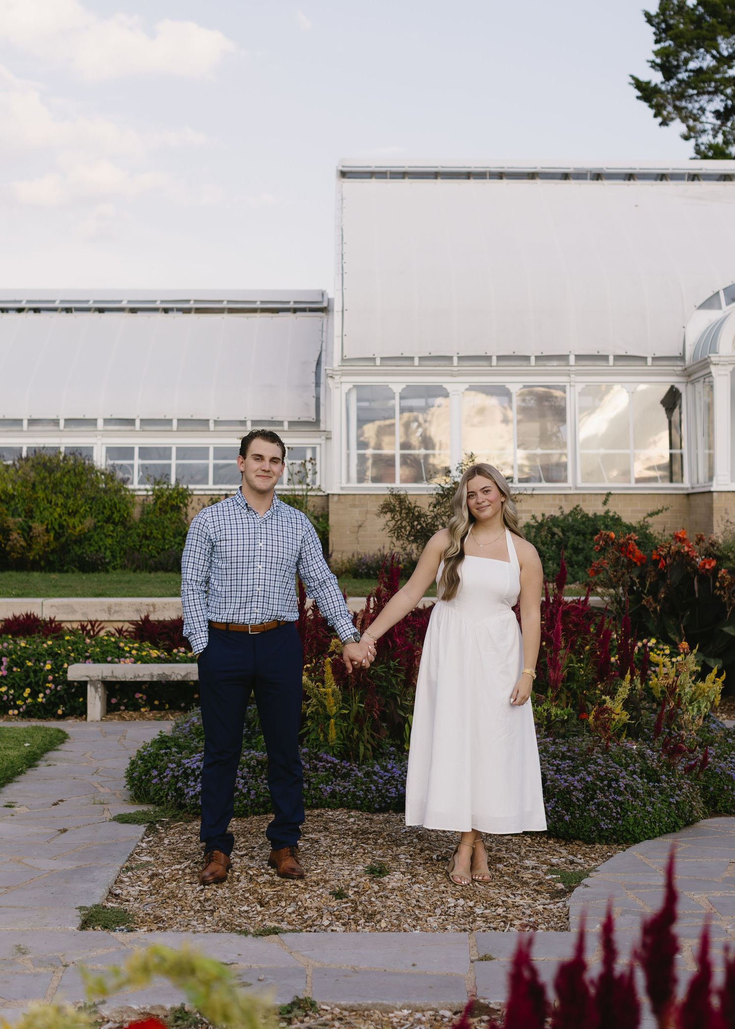 Elegant portrait session in a garden with architectural elements and burgundy florals in the foreground.