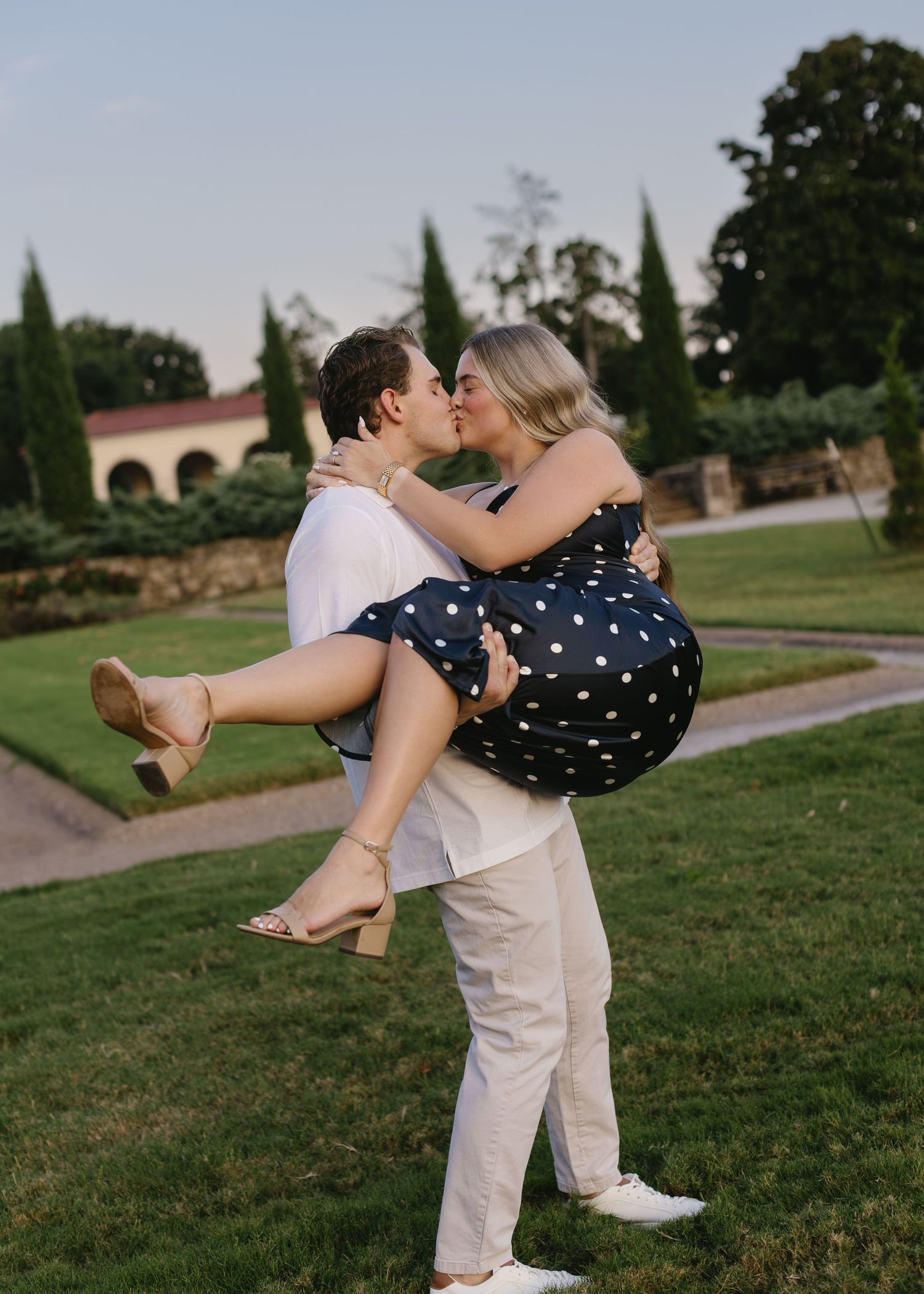 Romantic couple dancing in an outdoor garden setting with polka dot dress and light colored attire.