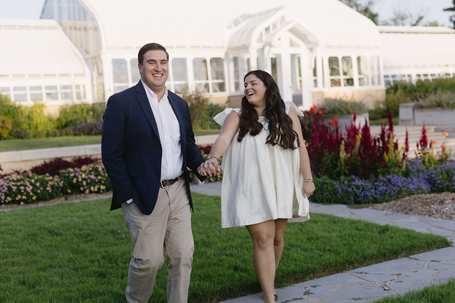 Couple takes romantic engagement photos in front of garden with blooming flowers.