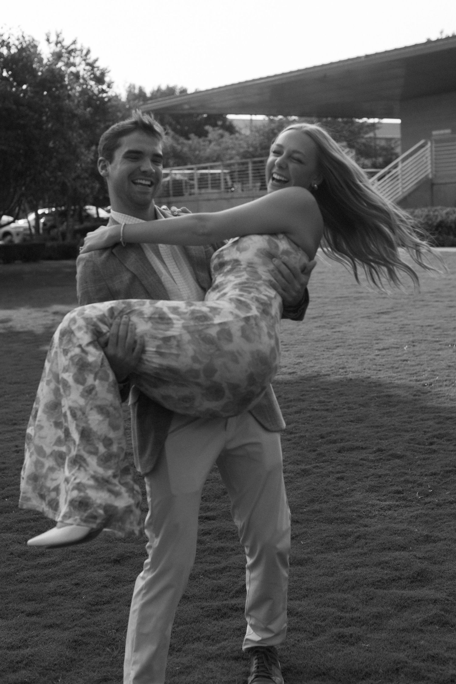 A playful couple dances and spins in a grassy field at sunset.