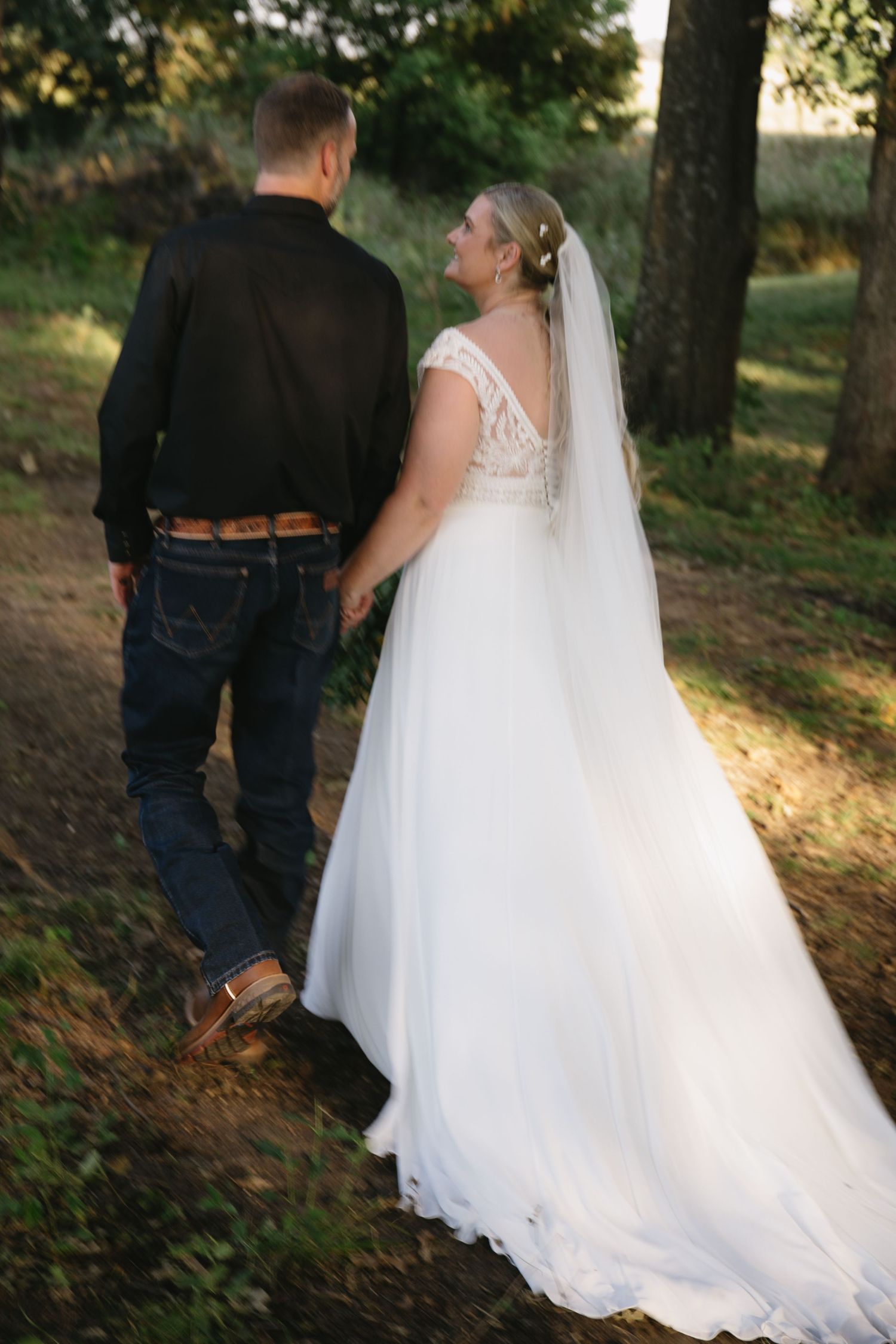 Romantic sunset portrait of newlyweds walking together on a wooded path.
