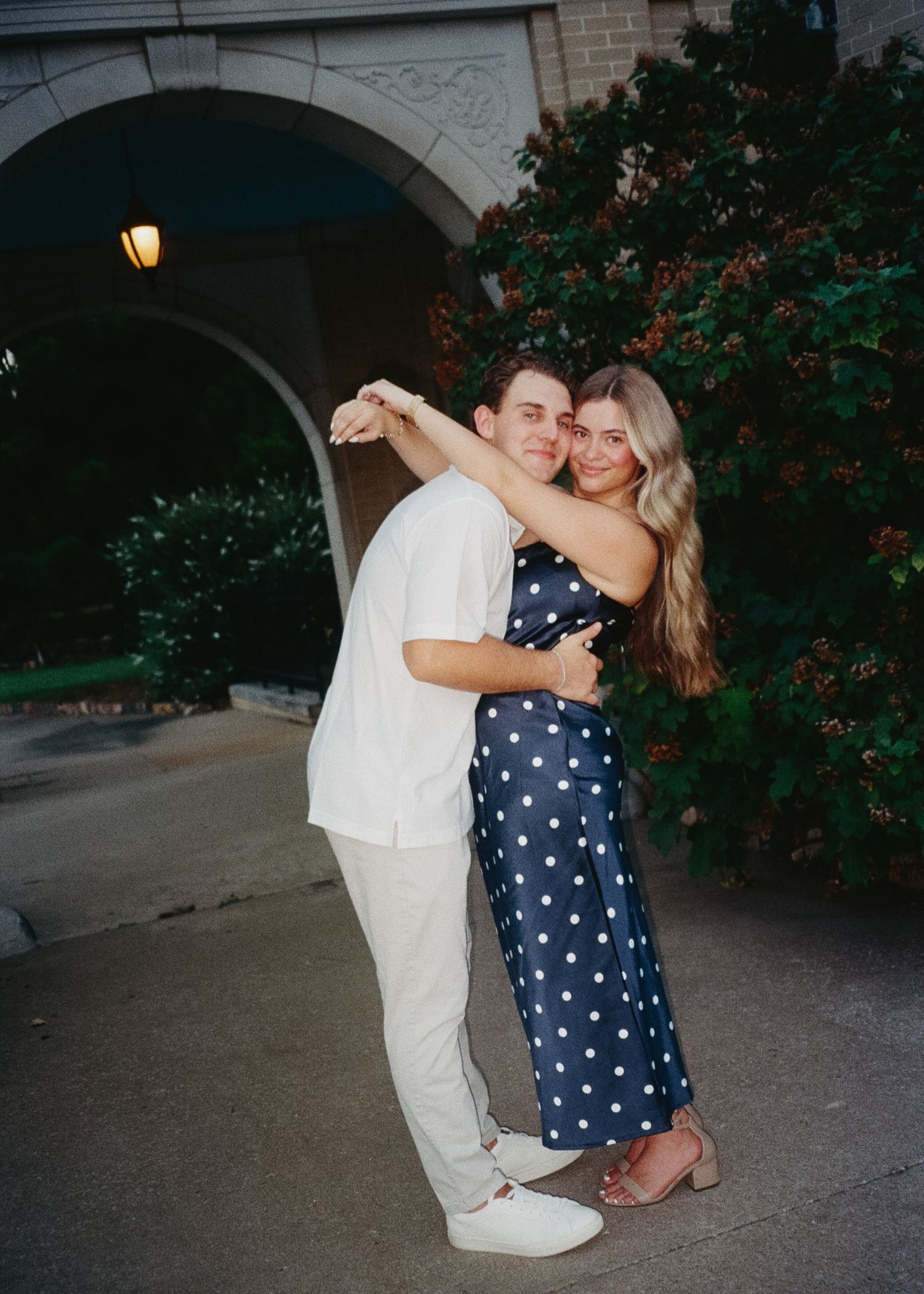 A couple embraces and dances together outdoors near blooming rose bushes and stone archways.