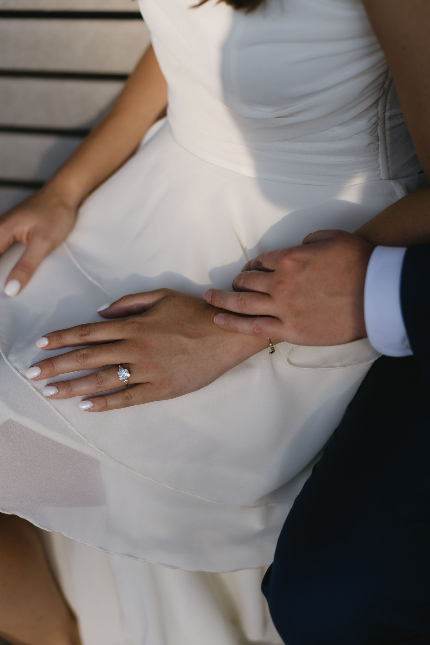 Close-up of hands displaying an engagement ring against a white dress fabric.
