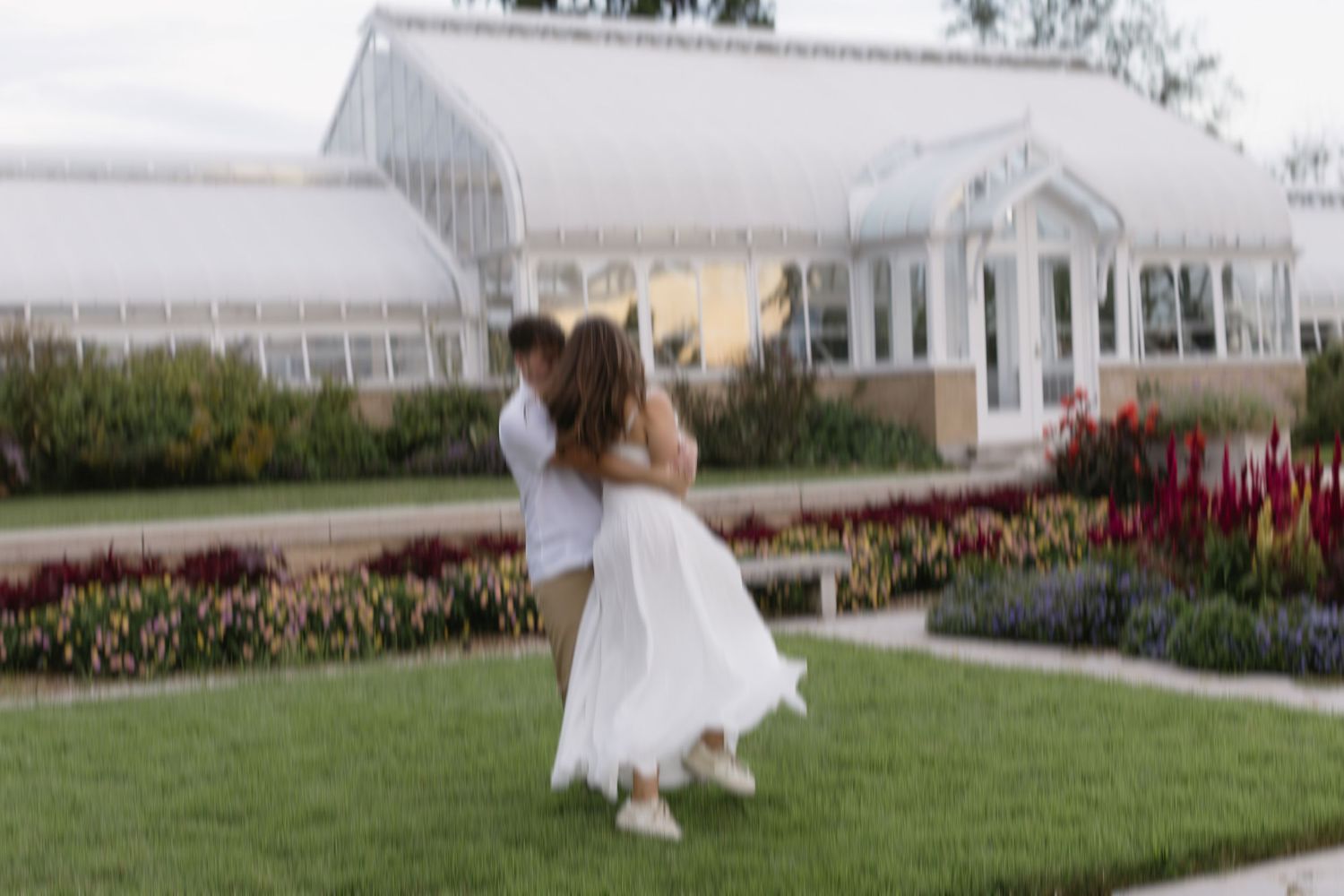 A wedding venue exterior featuring a white building with manicured gardens and red flowers along the path.