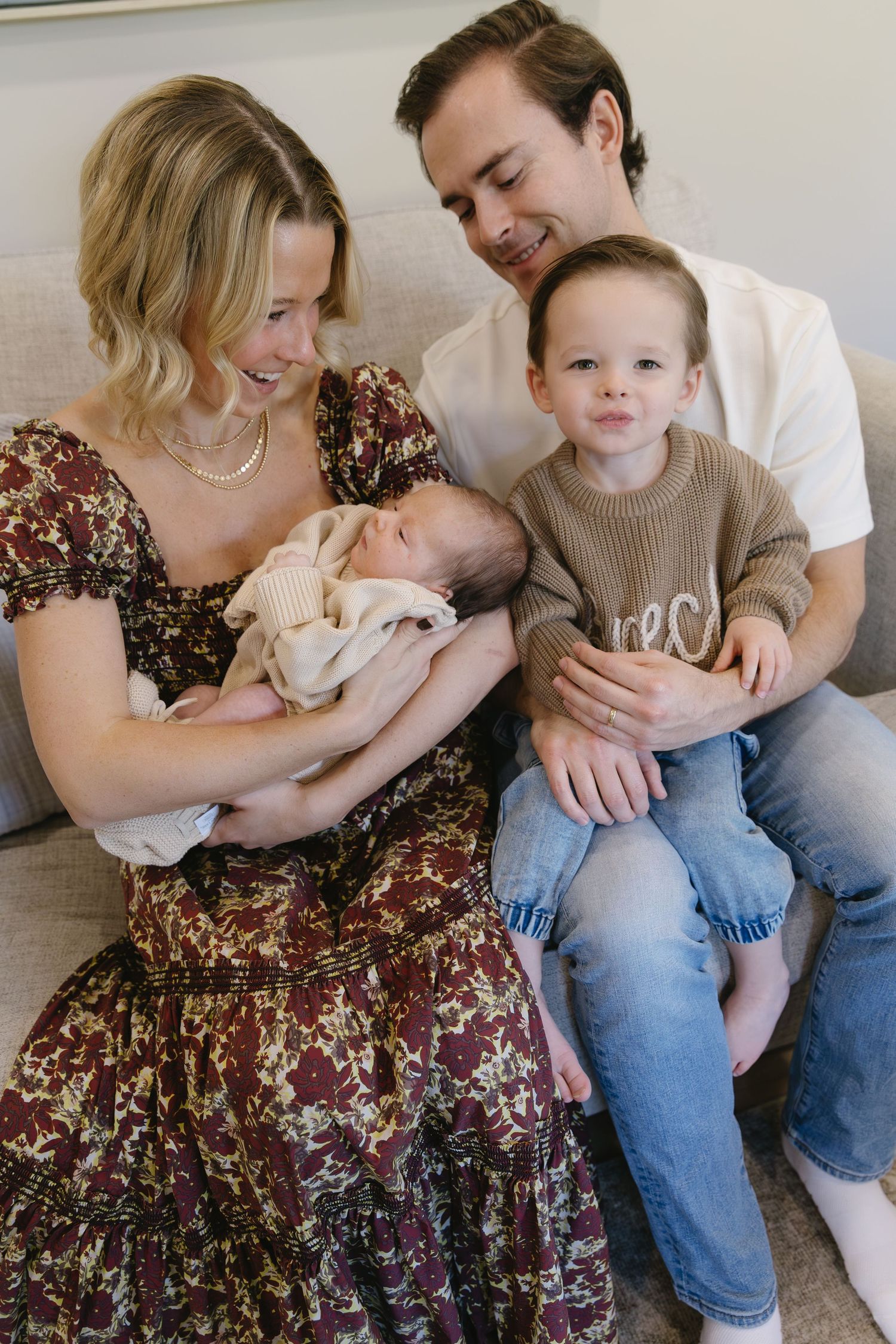 A family shares tender moments on a couch, wearing casual clothes and embracing a newborn baby.
