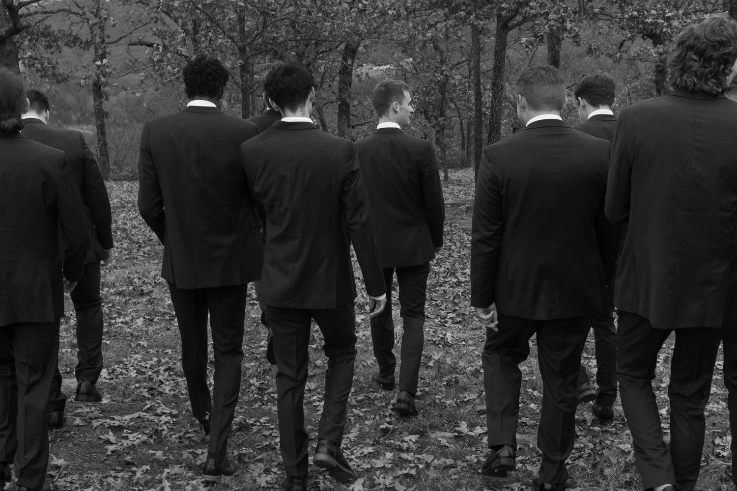 Black and white shot of groomsmen lined up in formal suits at outdoor wedding.
