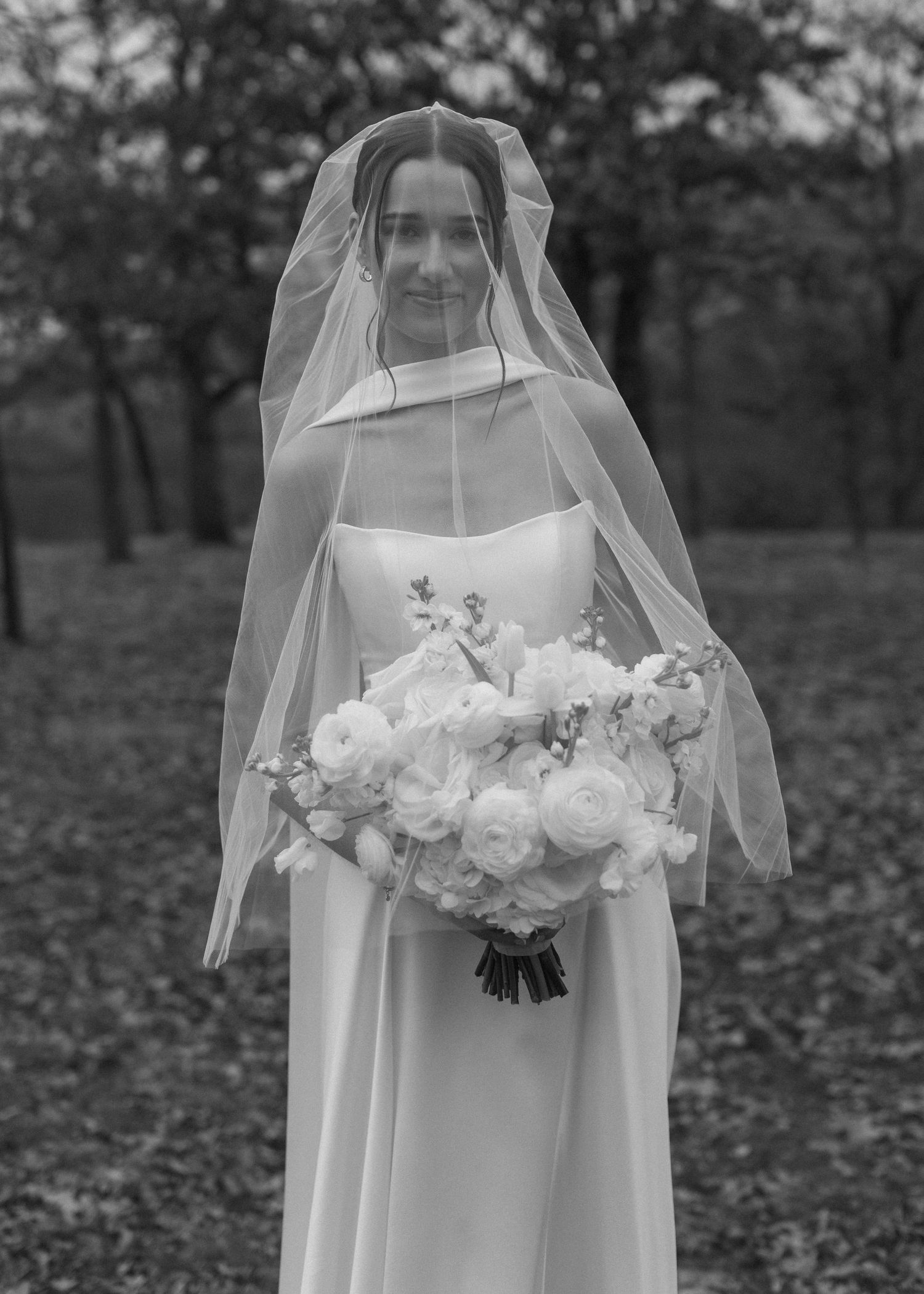 Elegant bride holds white rose bouquet during autumn outdoor wedding.