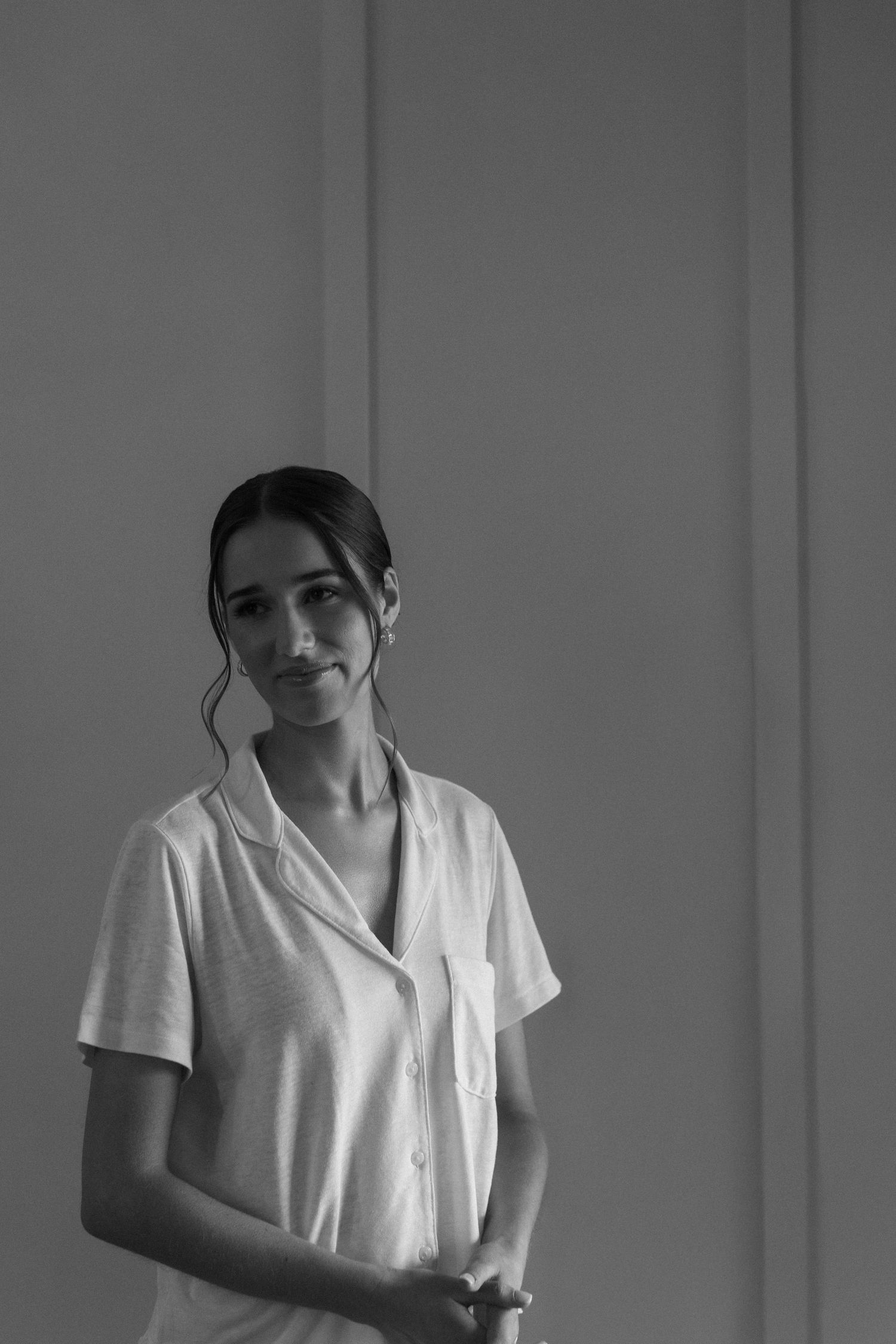 A woman in a white collared shirt smiles softly in a minimalist black and white portrait.
