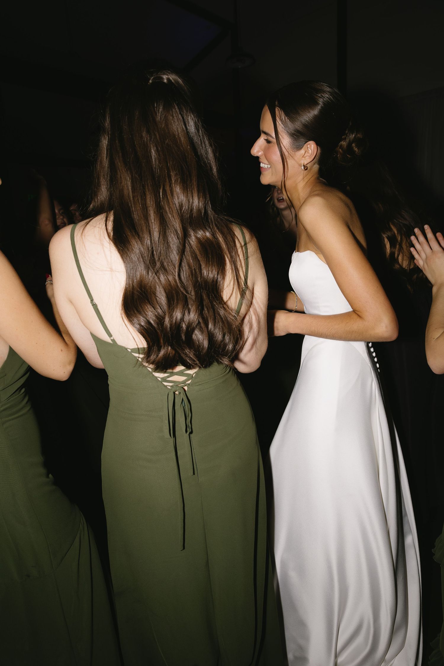 Line of bridesmaids in olive green and white dresses shown from behind.